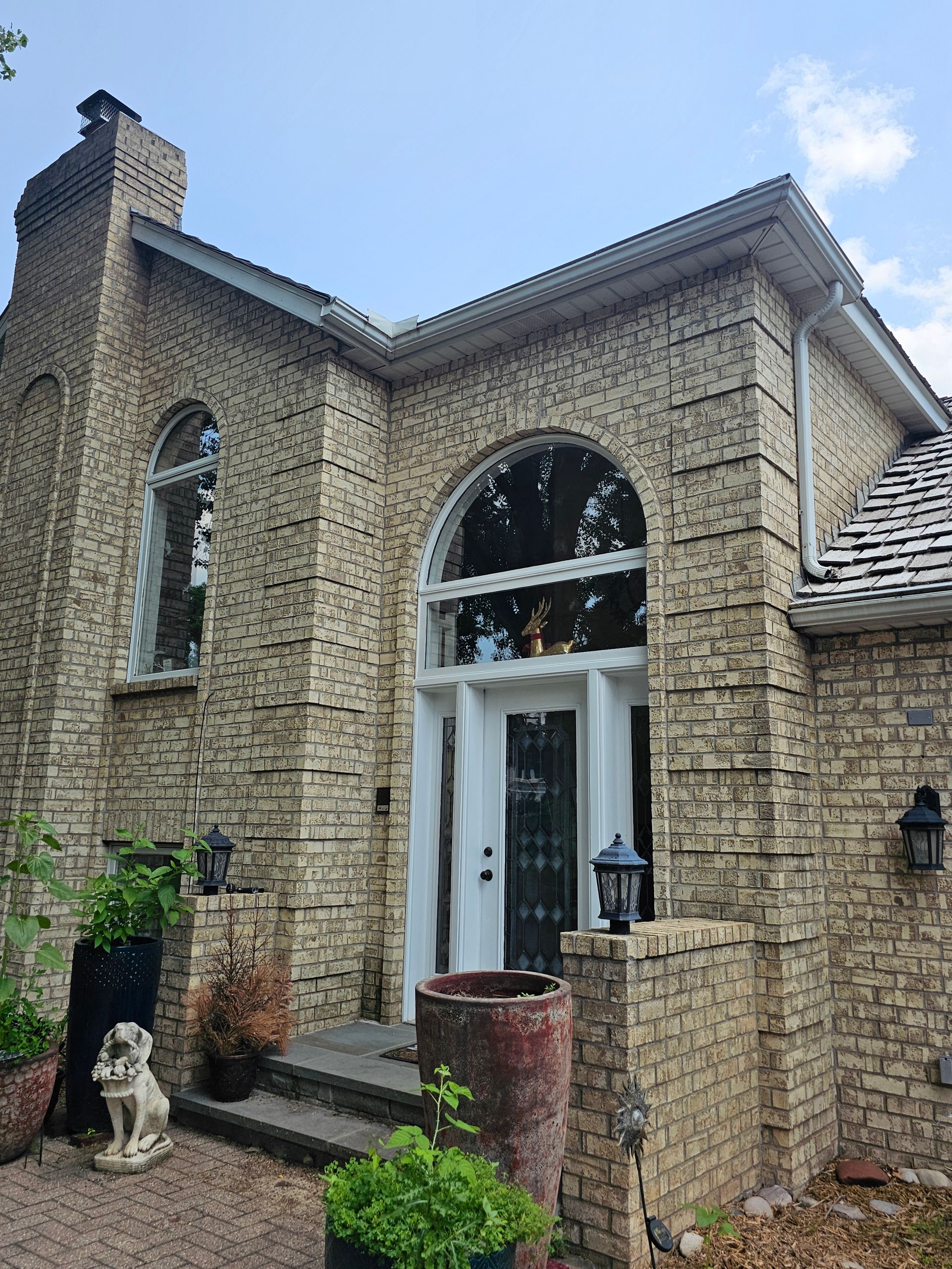 Brick house with arched doorway, white door, and arched window. Dark shutters, blue sky.