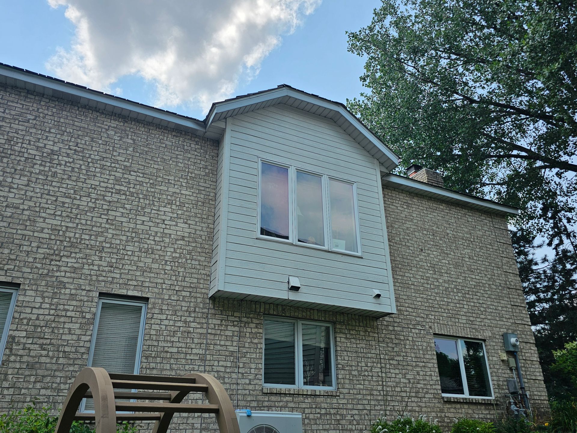 Tan brick building with windows, a light-colored bump-out, and a cloudy sky in the background.