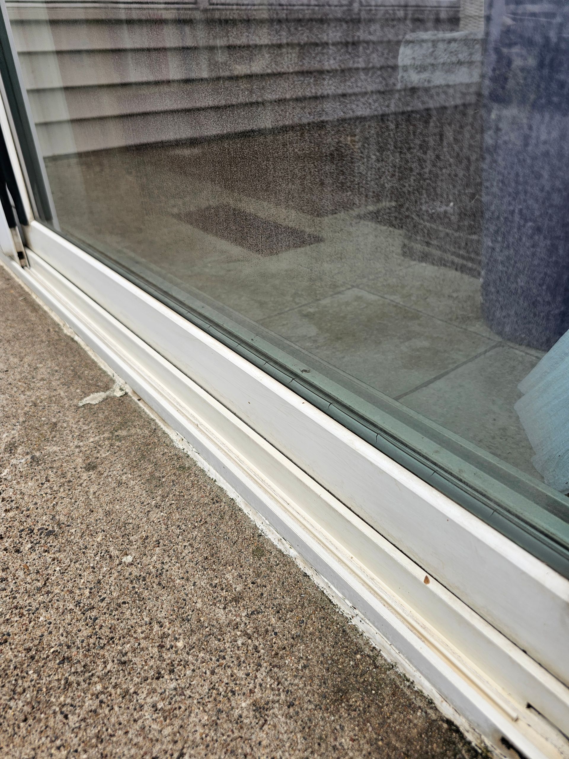 White sliding glass door frame on a gravel surface. The glass reflects a blurry interior and steps.