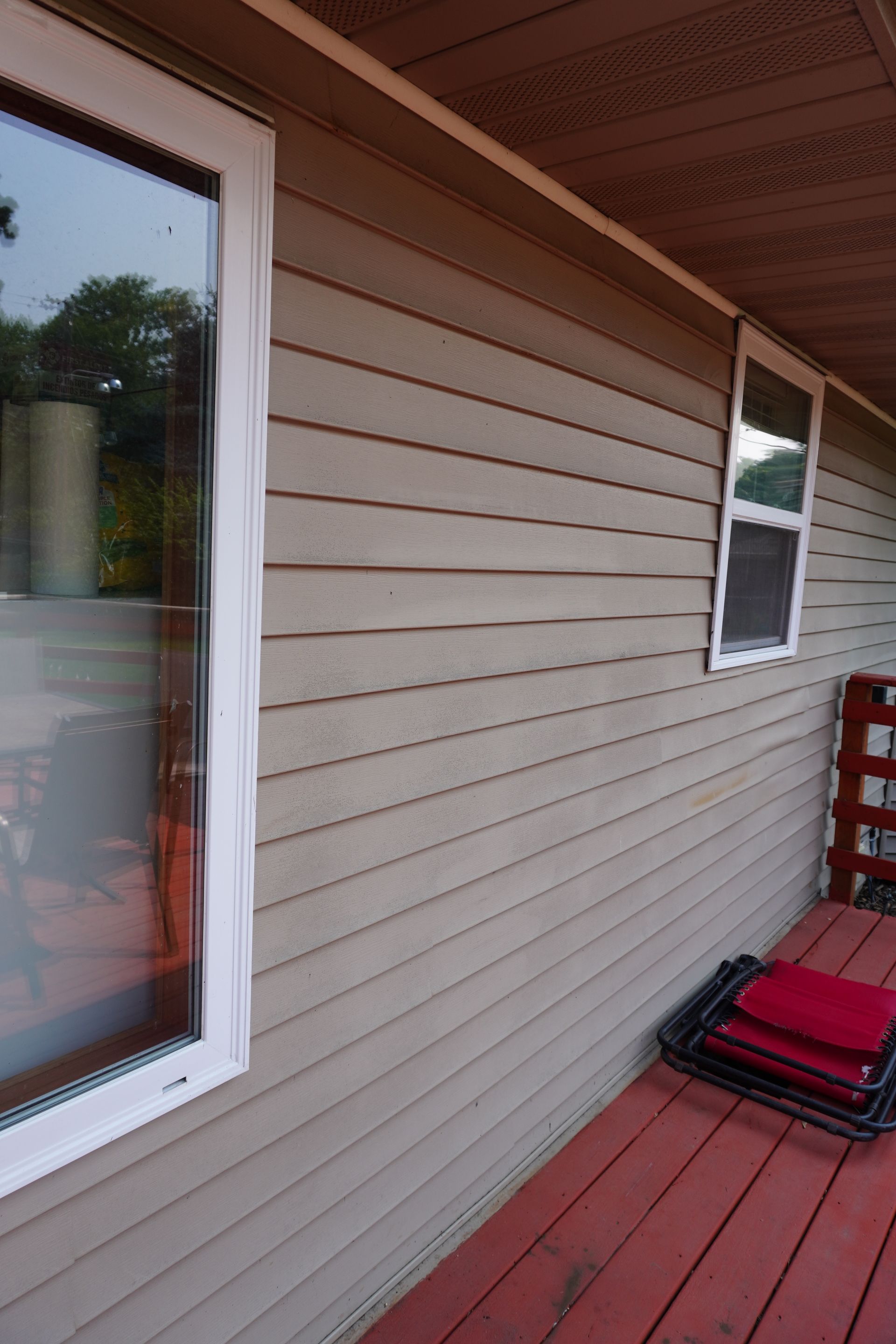 Side of a house with light brown siding, white-framed windows, and a red deck with chairs.