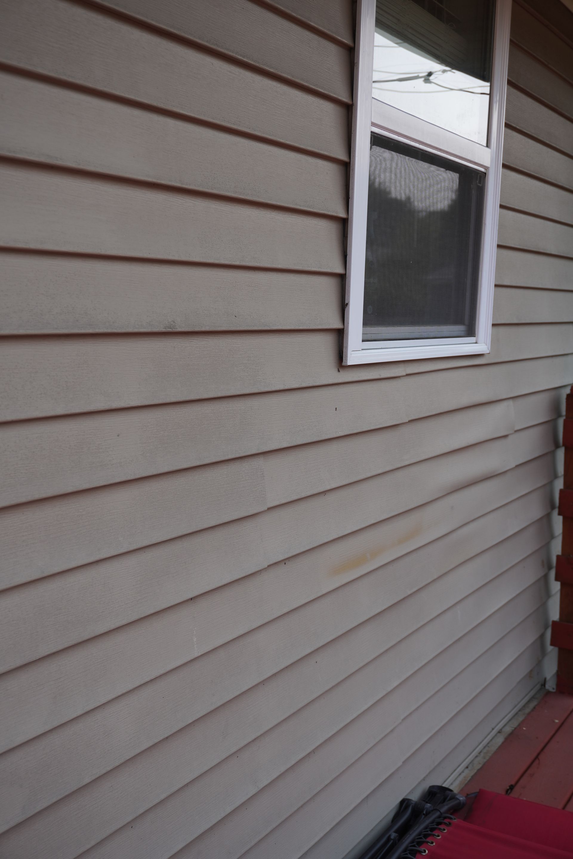 Tan siding on a building with a window. Dark area below the window.