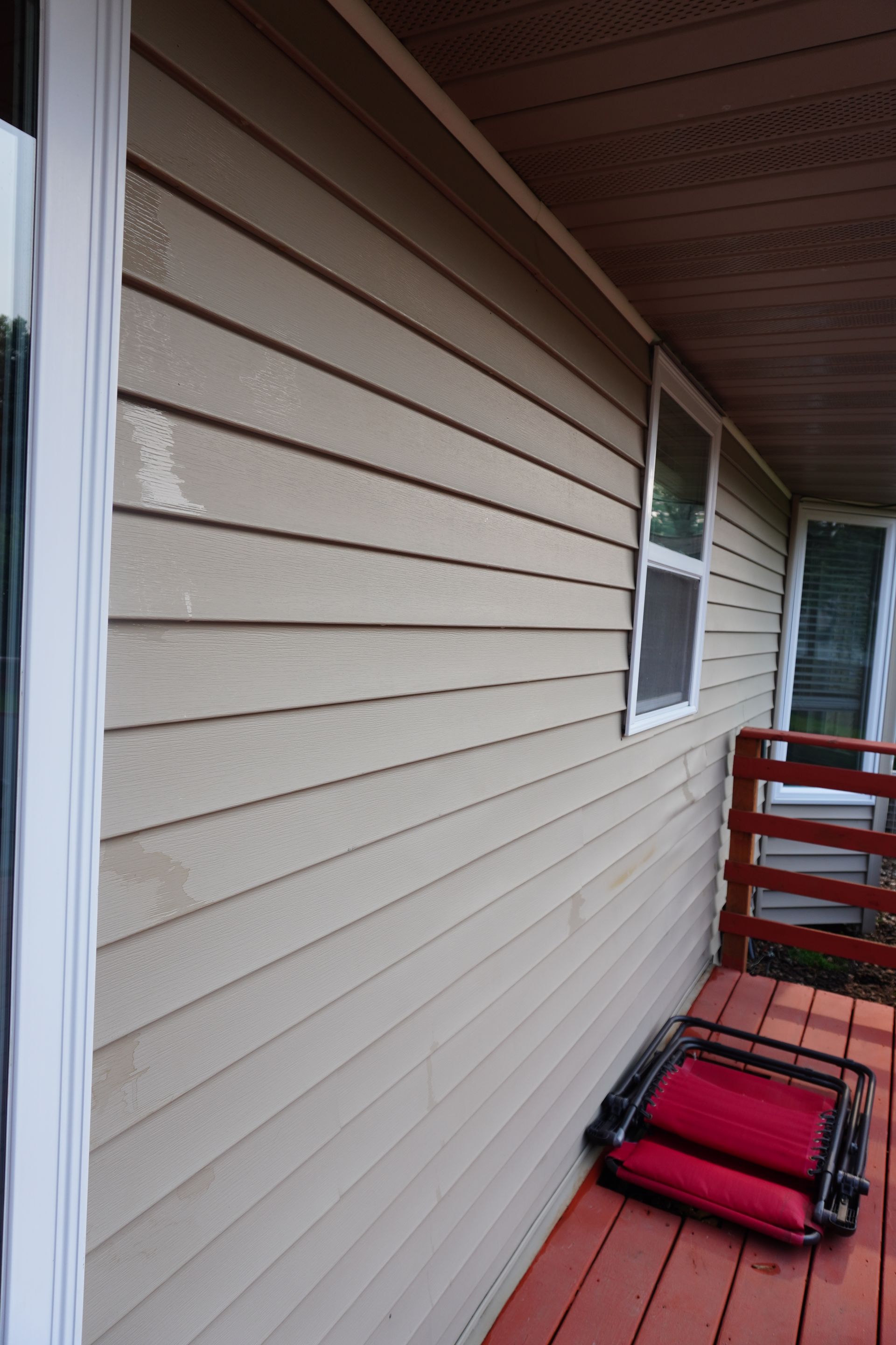 Beige siding on a house exterior with a red deck, a small window, and a folded red chair.