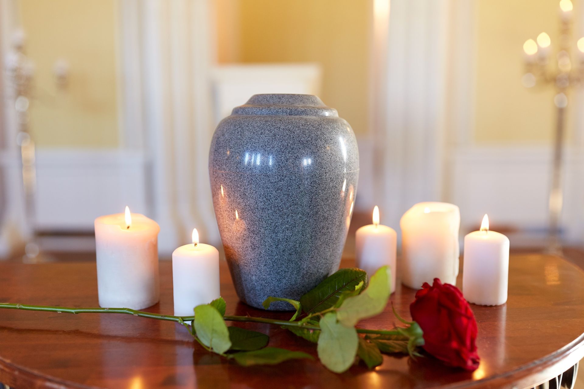 Memorial urn displayed with lit candles and a single red rose on a table.