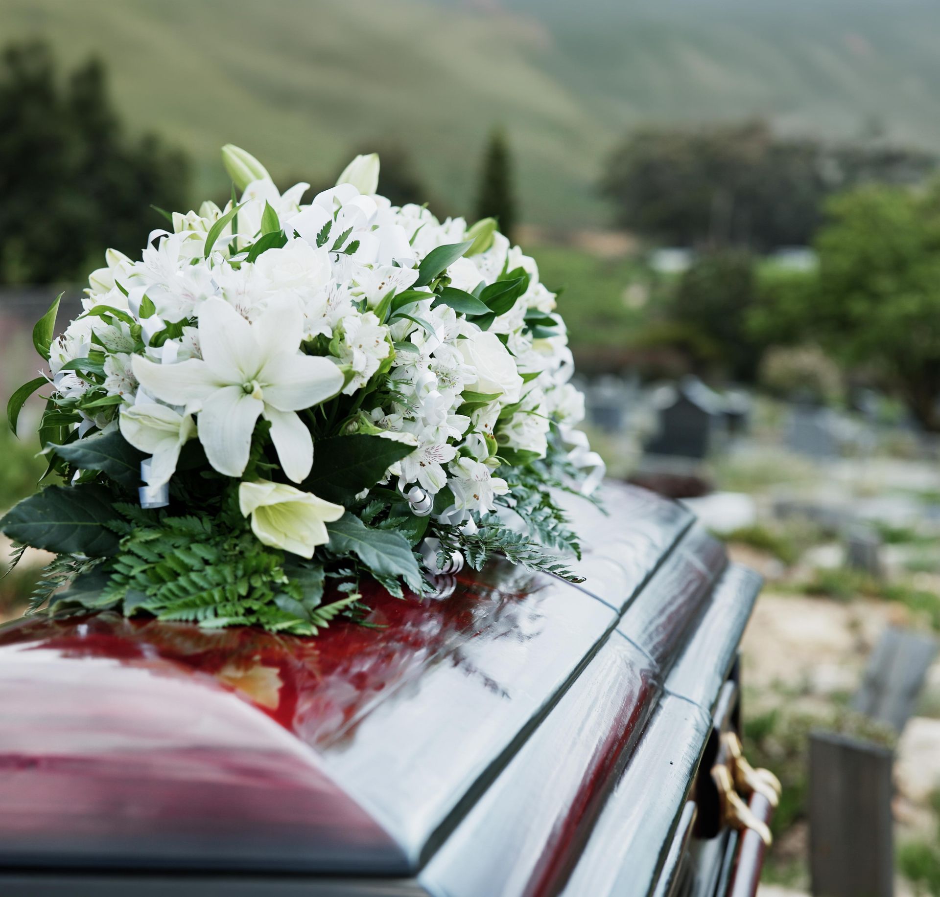 White flower bouquet on a casket outdoors with blurred green hills in the background