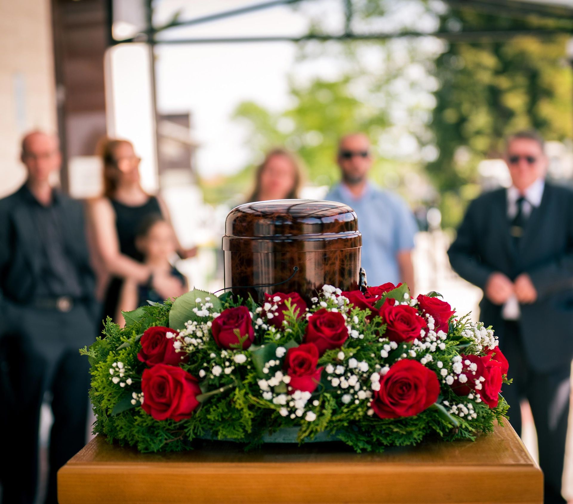 A cremation urn surrounded by red roses on a wooden table during a memorial service