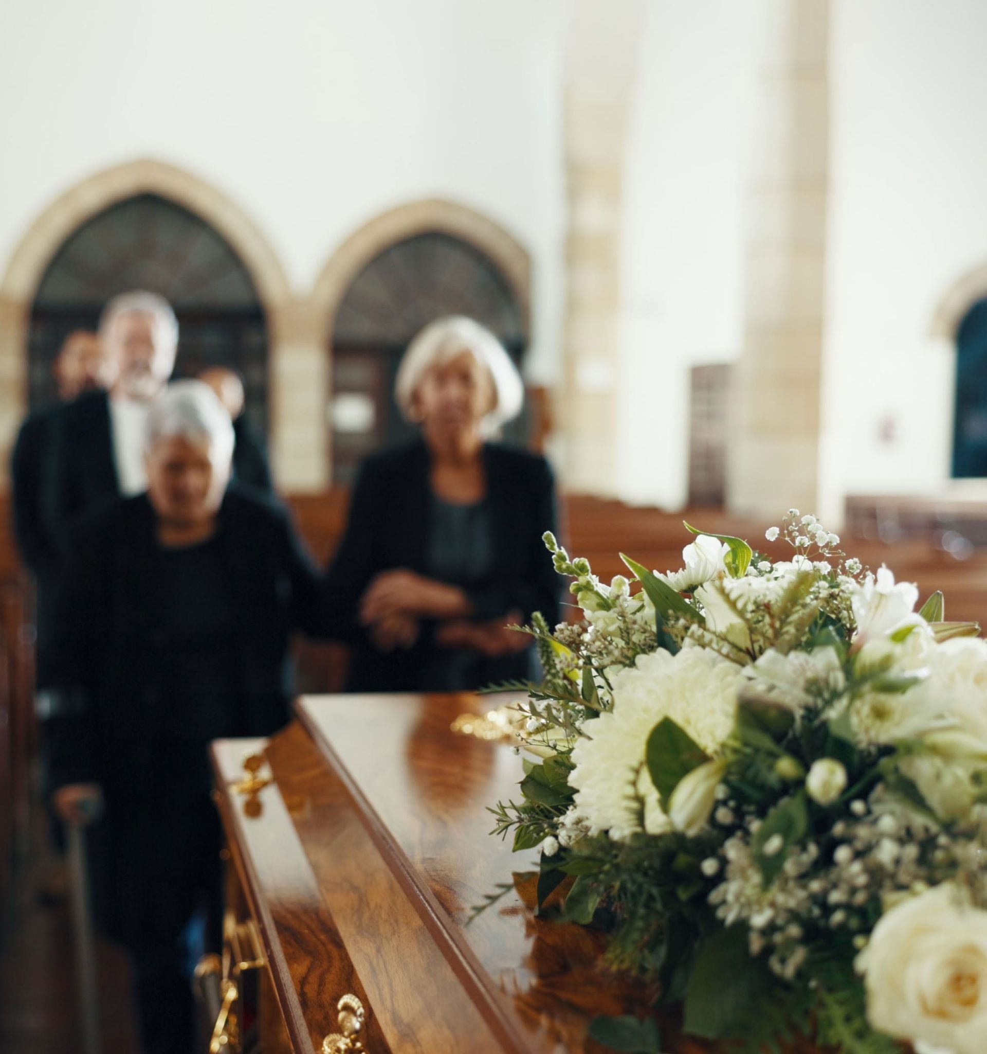 Flower-covered coffin being carried in a church aisle by mourners