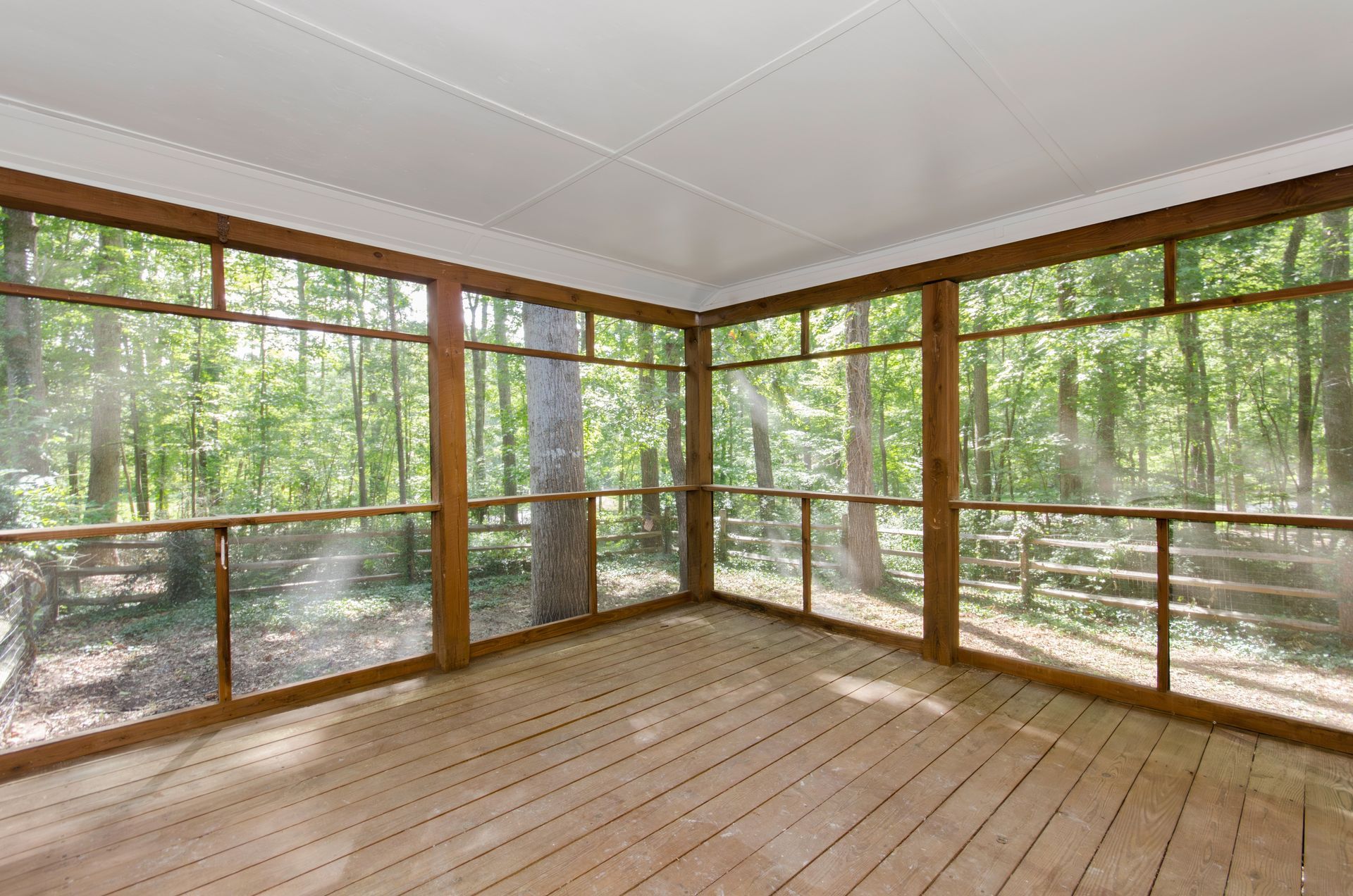 Screened-in porch with wood floors and trim, looking out at a forest of green trees.