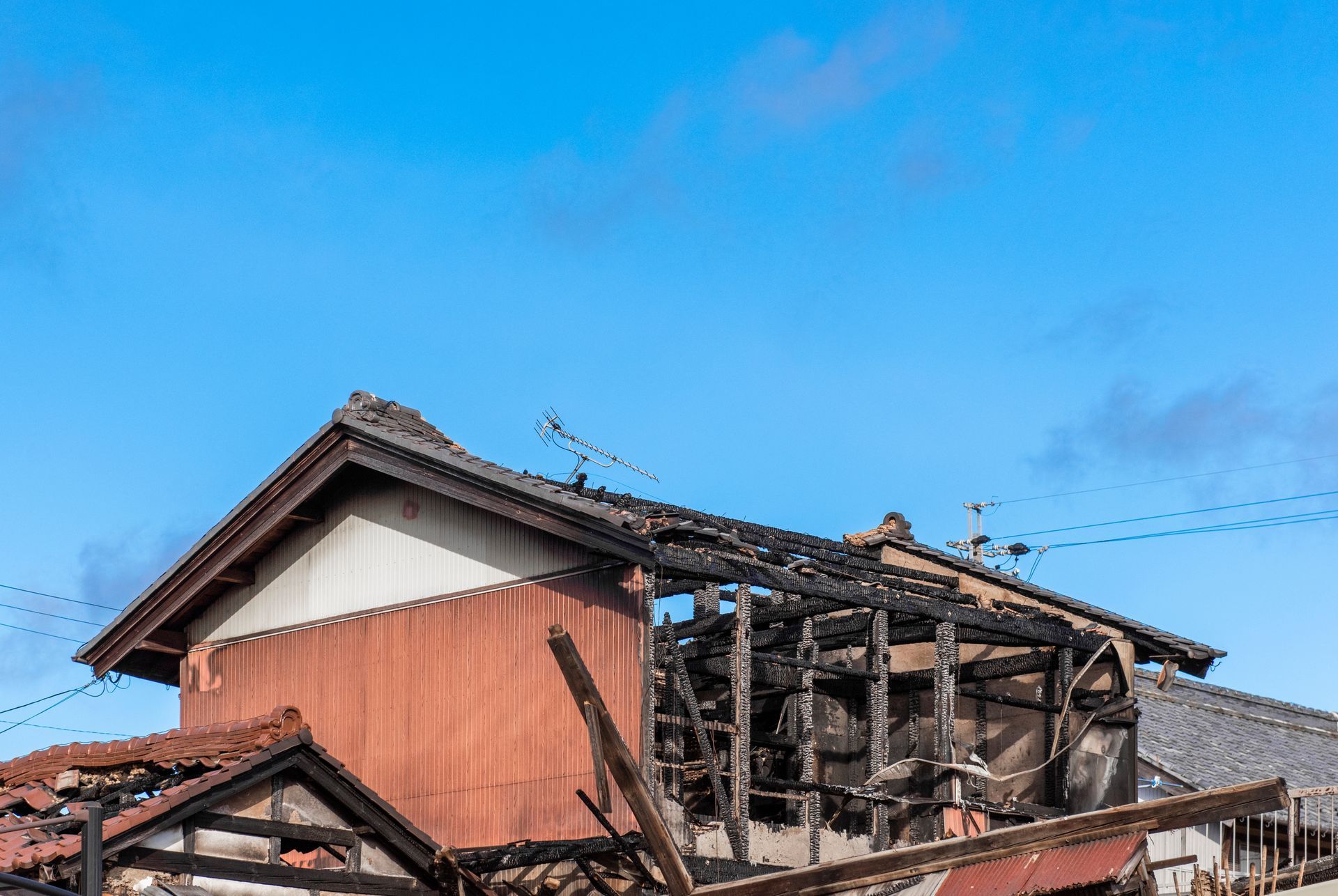 Partially burned wooden building with charred roof against blue sky.