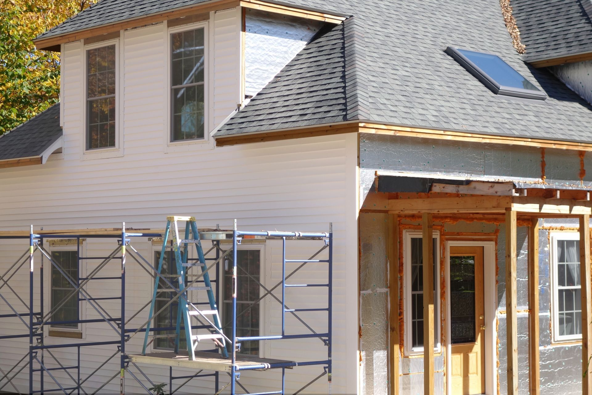 House under construction; scaffolding, partially finished siding, exposed framing, and skylight.