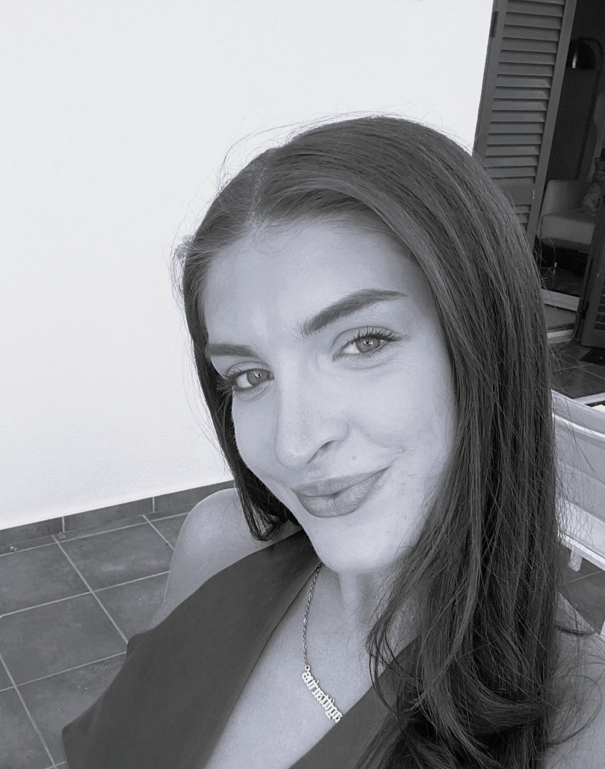 Close-up black-and-white selfie of a smiling person indoors, with a tiled floor and doorway behind them
