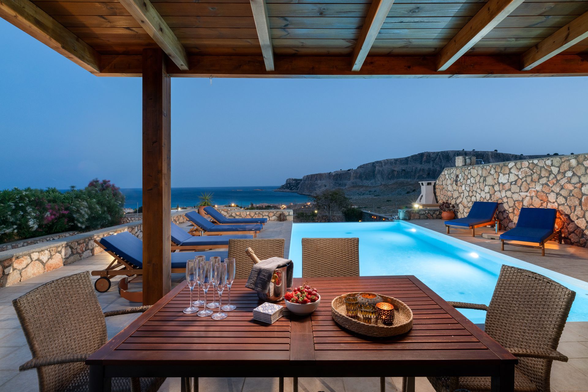Covered patio with dining table and infinity pool overlooking the ocean at sunset