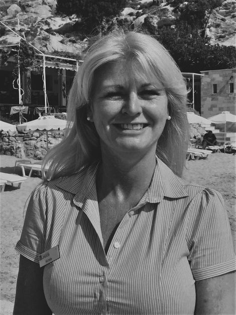 Smiling person standing outdoors near a pool, with trees and lounge chairs in the background.
