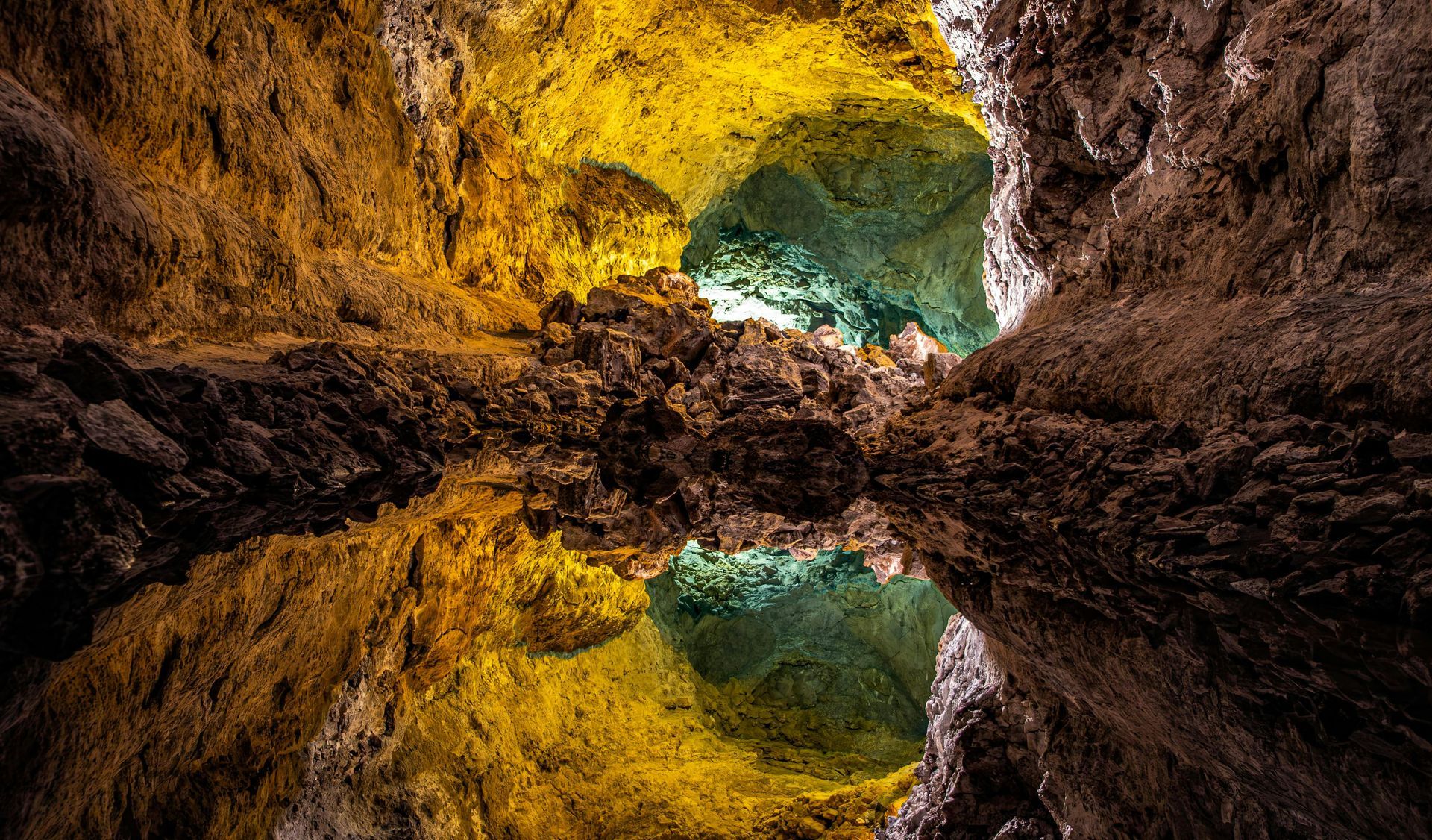 Reflective cave cavern with yellow, brown, and turquoise rock and water