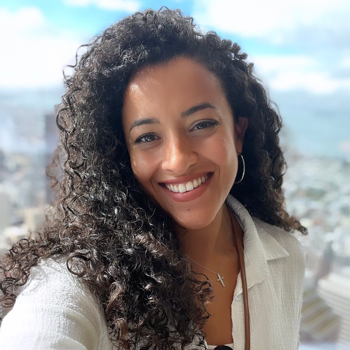 A woman with curly hair is smiling and wearing a white shirt.