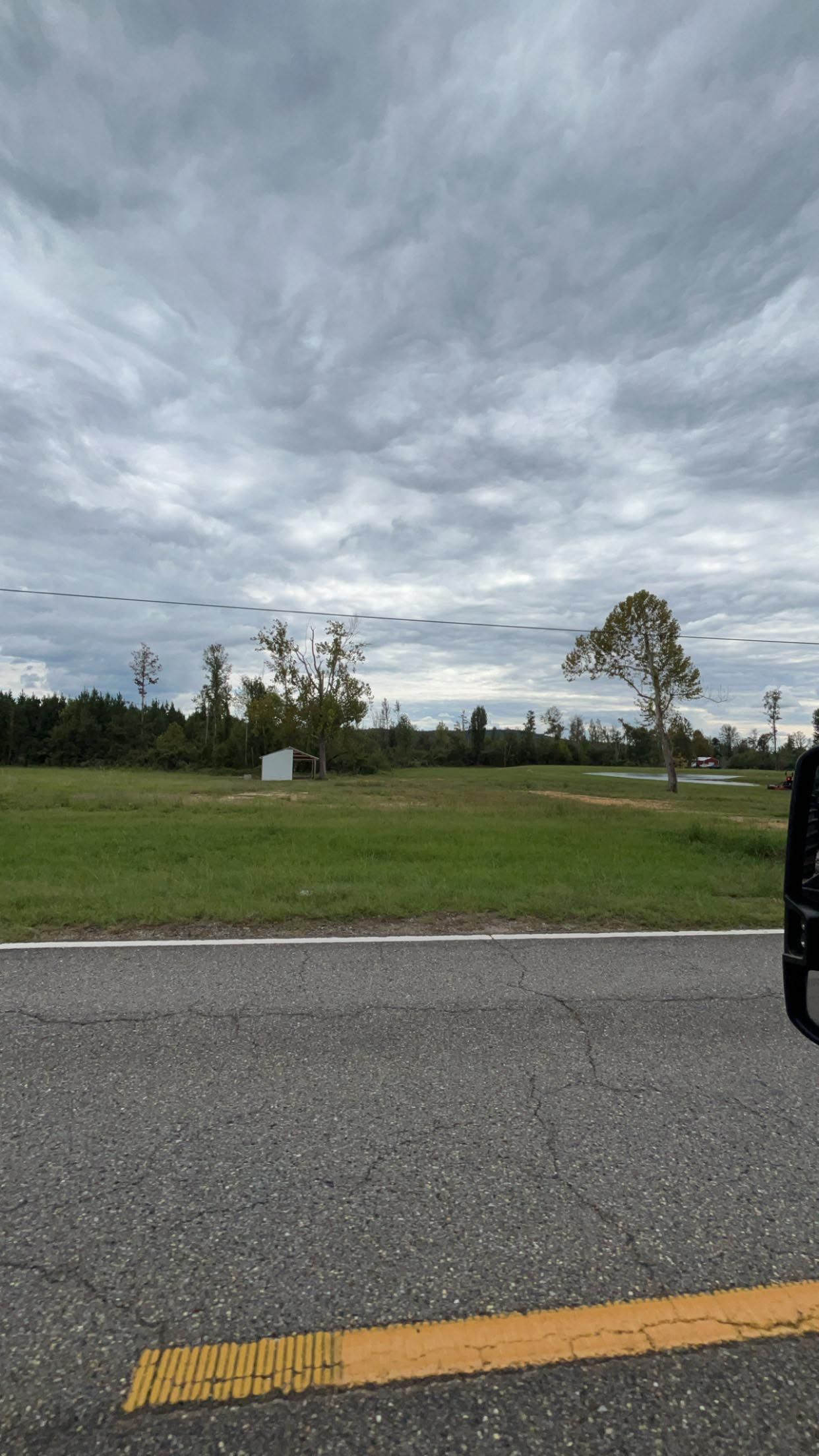 A road with a yellow line on the side of it and a field in the background.
