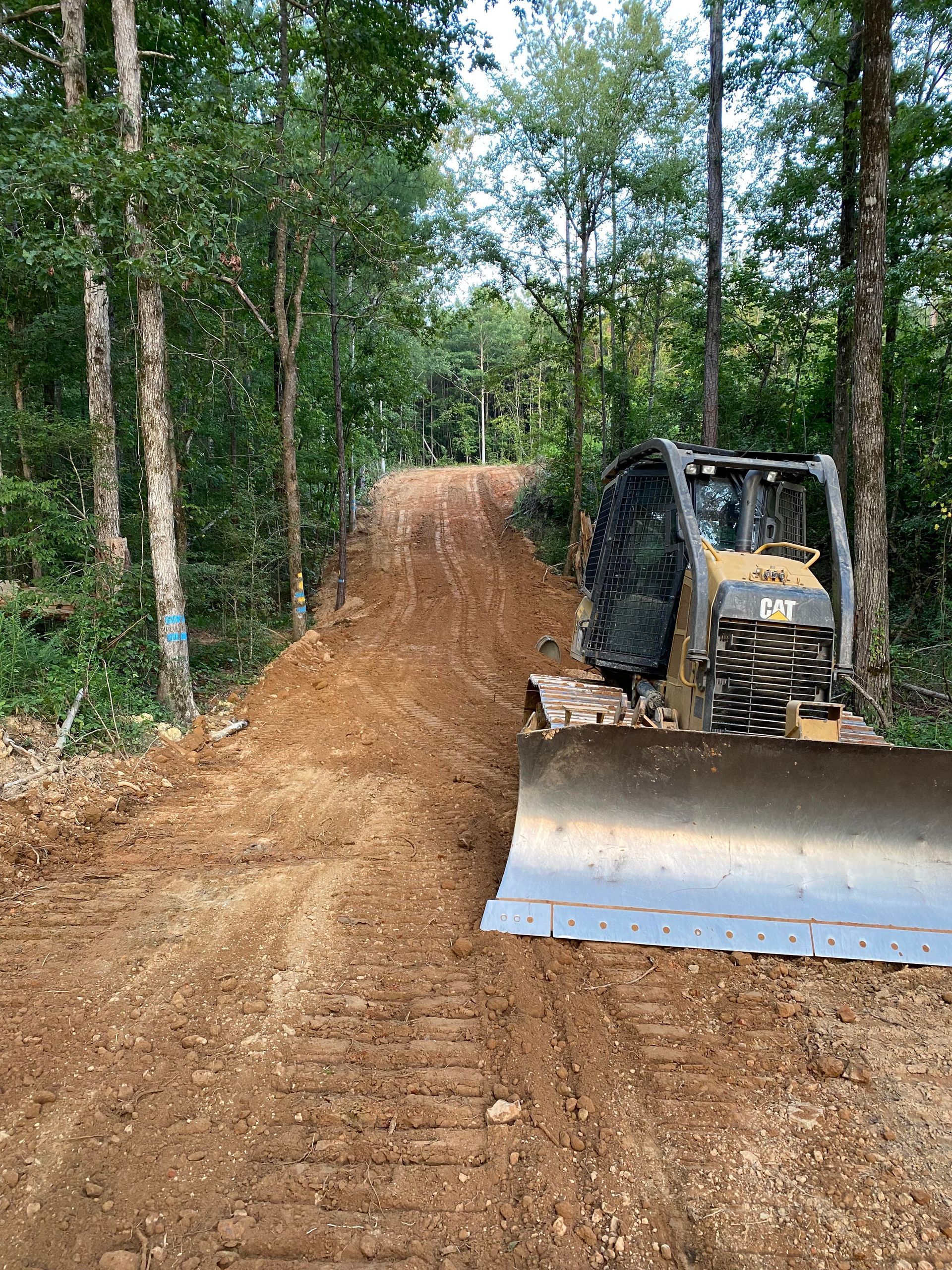 A bulldozer is driving down a dirt road in the woods.