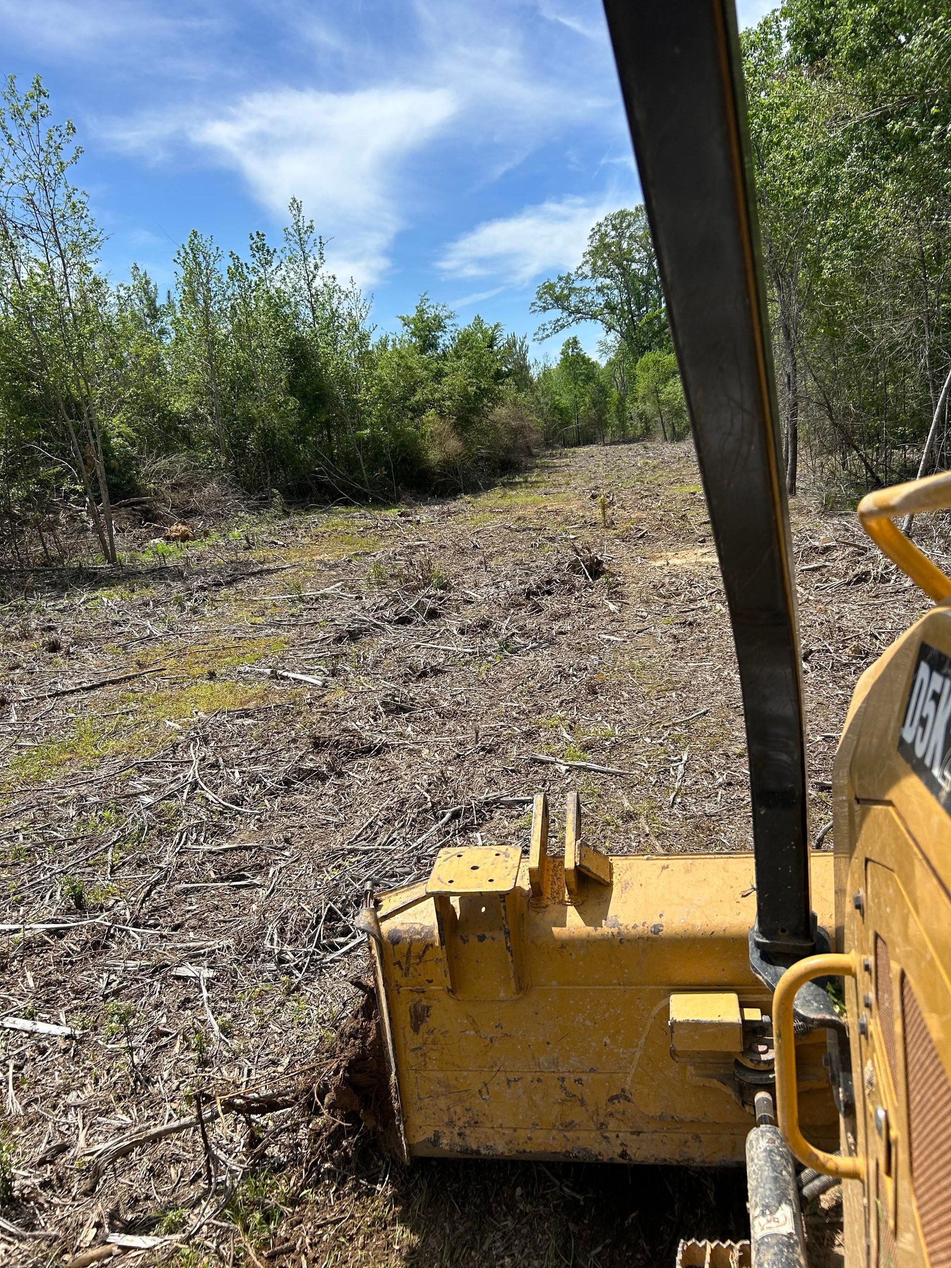 A yellow bulldozer is cutting down trees in a field.