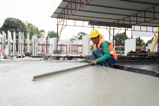Construction worker leveling wet concrete with a long screed in a partially built structure