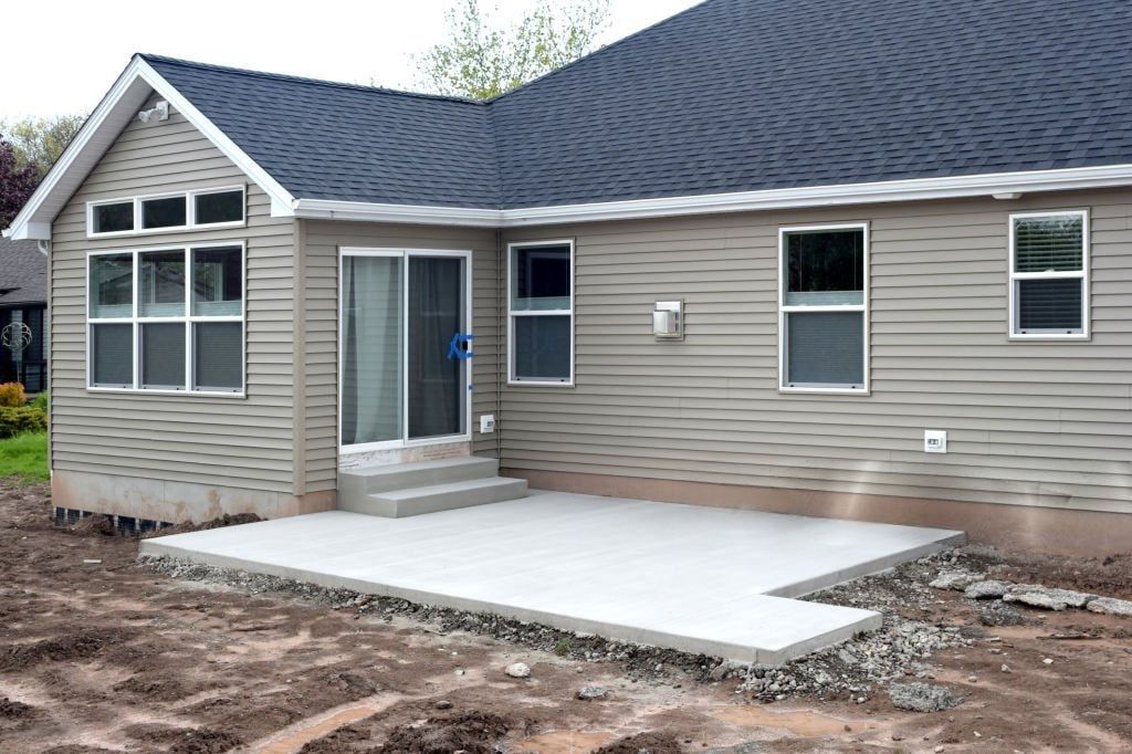 Single-story beige house with a dark roof and a concrete front patio under construction
