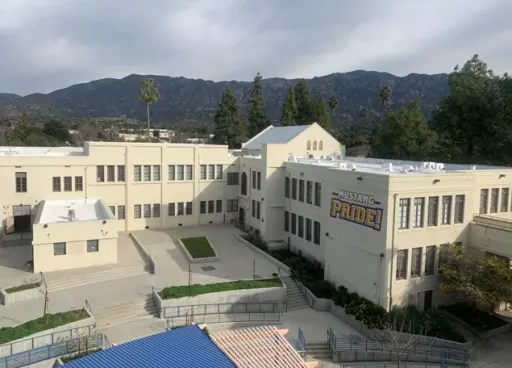 Commercial building with tan and white facade, windows, and parking spaces. Blue sky and greenery.