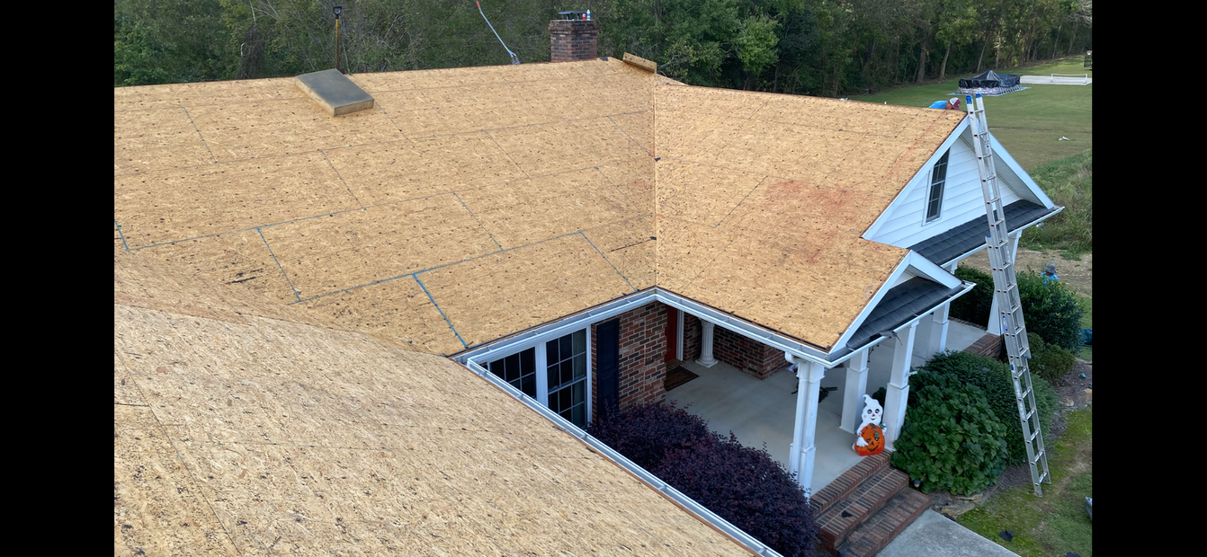 An aerial view of a house roof undergoing renovation with new plywood sheathing and a ladder resting against the porch.