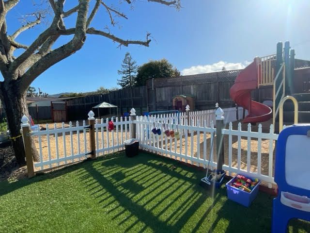 Exterior view of Alpha Kids Academy day care center playground with white picket fence and lawn
