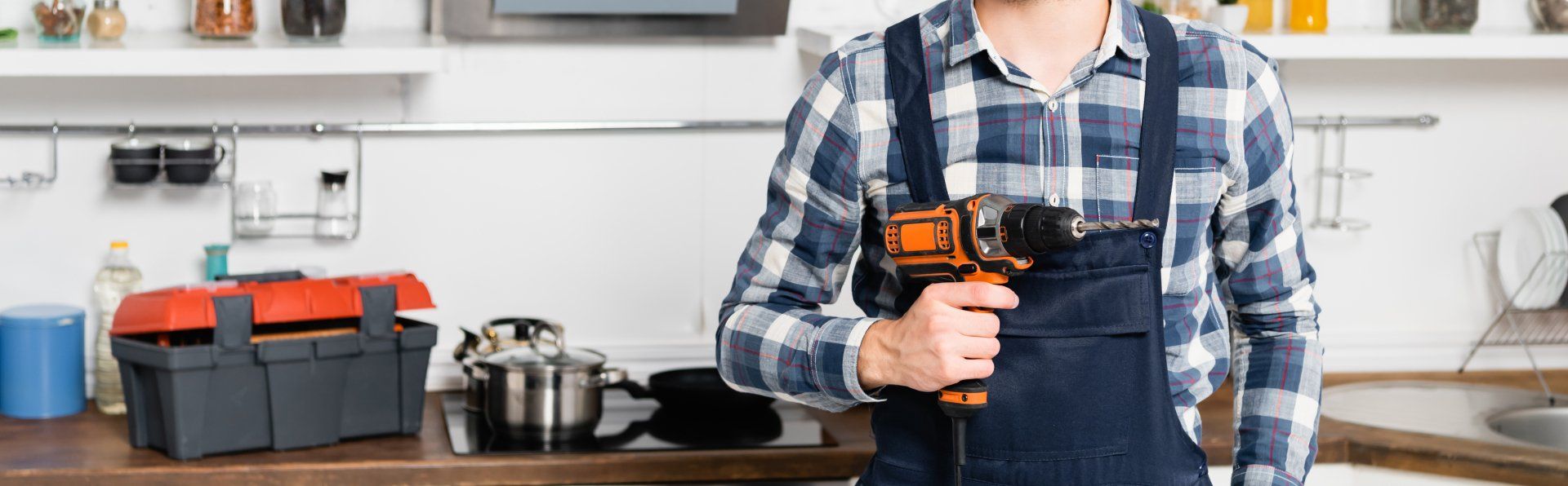 cropped view of handyman holding drill on blurred background in kitchen, banner