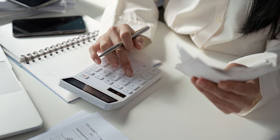 Person using a calculator while holding papers, possibly reviewing financial documents at a desk.