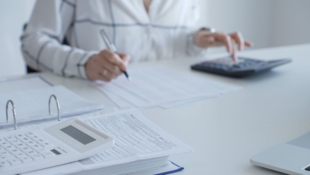 Woman using calculator and pen at a desk with paperwork and binder.