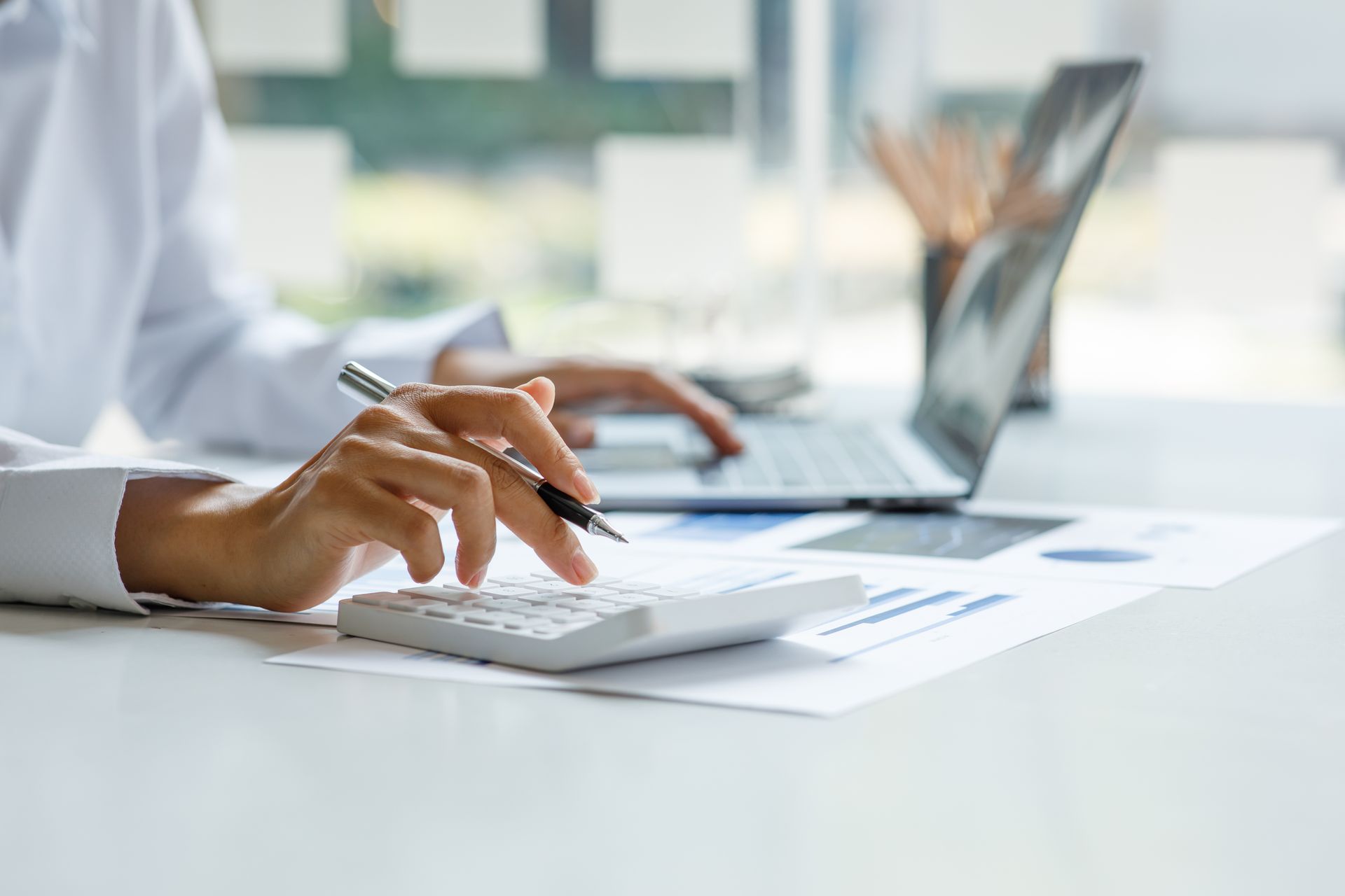 Person using a calculator and laptop at a desk with financial documents.