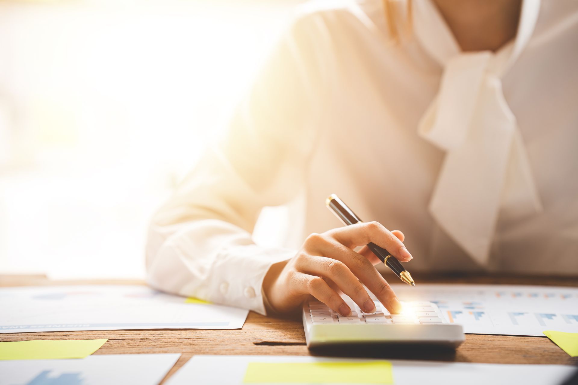 Woman in white blouse using a calculator with documents on a wooden desk.