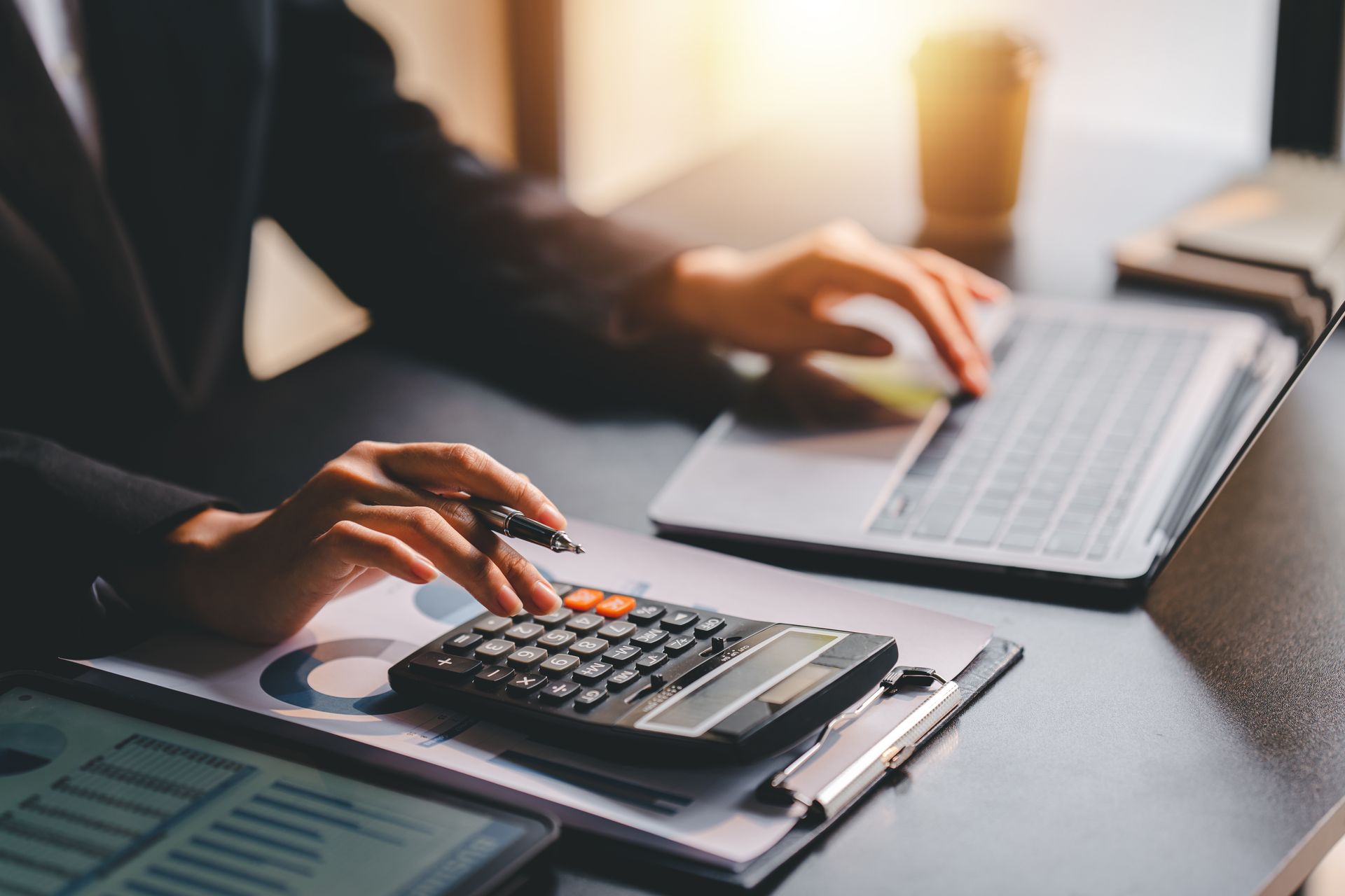 Person using a calculator and laptop, working at a desk with financial documents.
