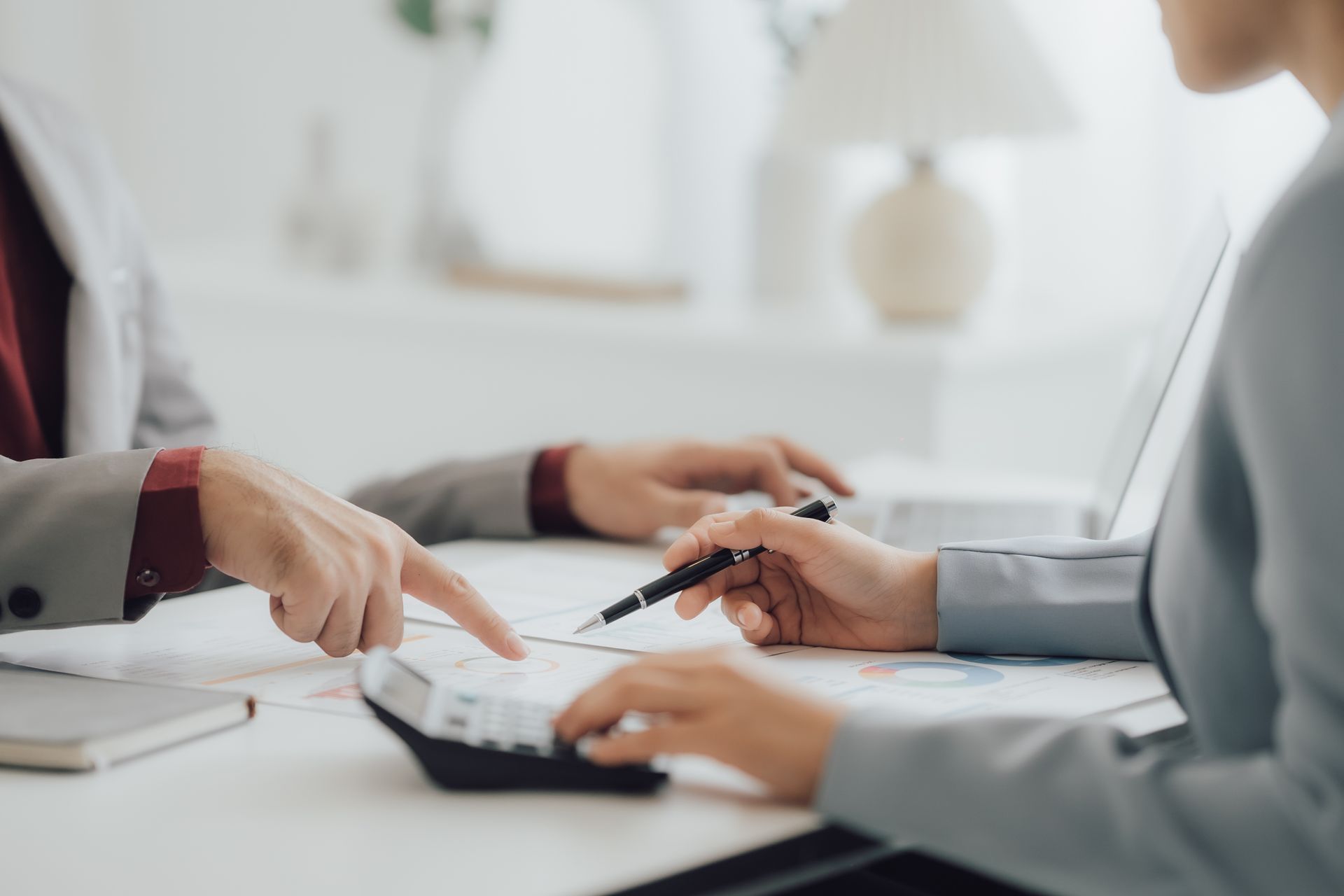 Two people reviewing financial documents, using a calculator, with hands pointing and gesturing.