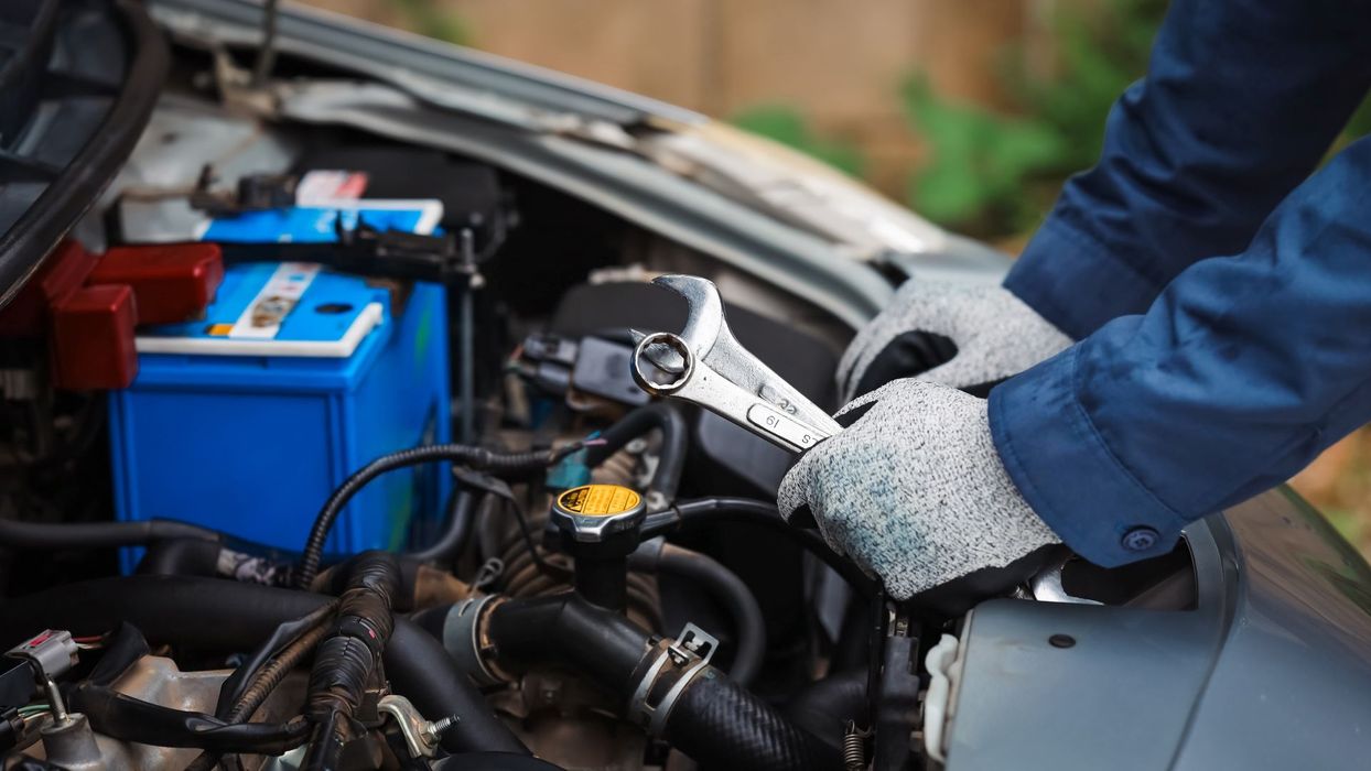 Hands in work gloves using a wrench on a car engine.