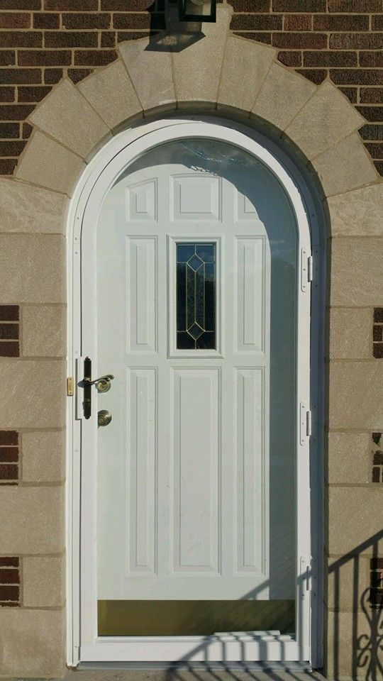 White arched door with small window set in a stone archway against brick facade.
