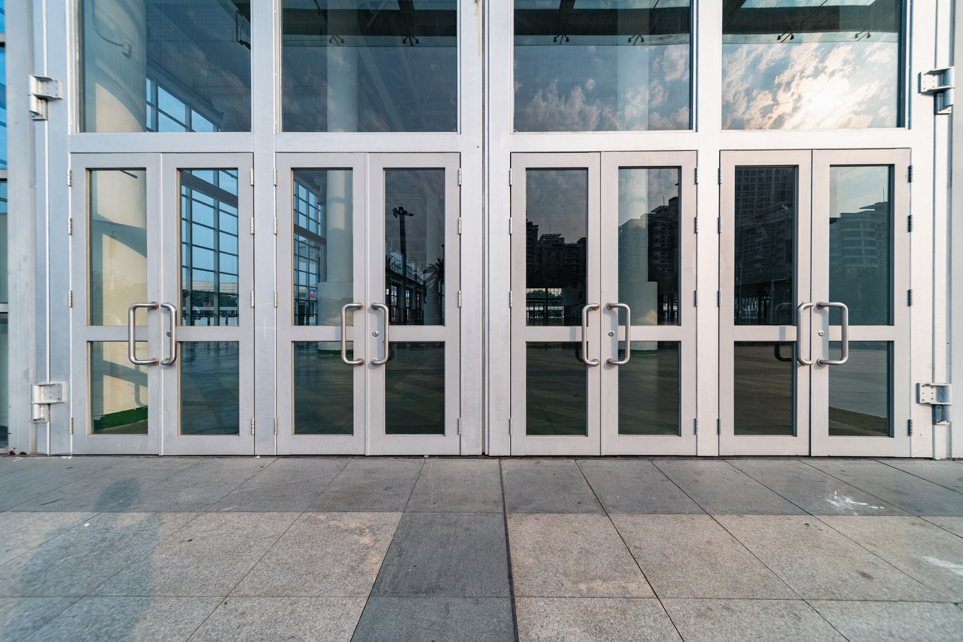 Exterior view of a building entrance with glass doors. Gray doors and silver frames, set in concrete.