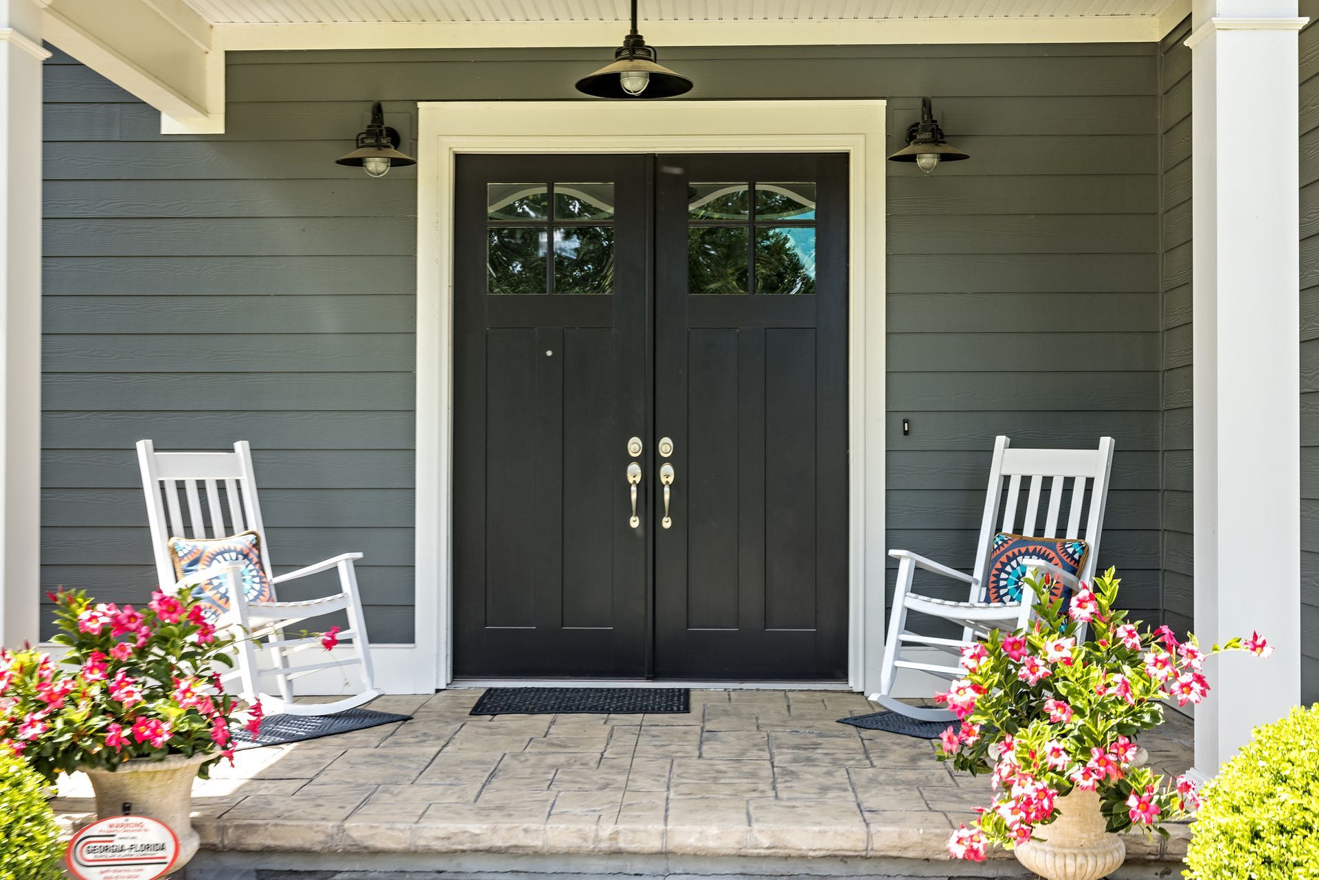 Black double entry doors with glass panels framed by porch decor and white rocking chairs.