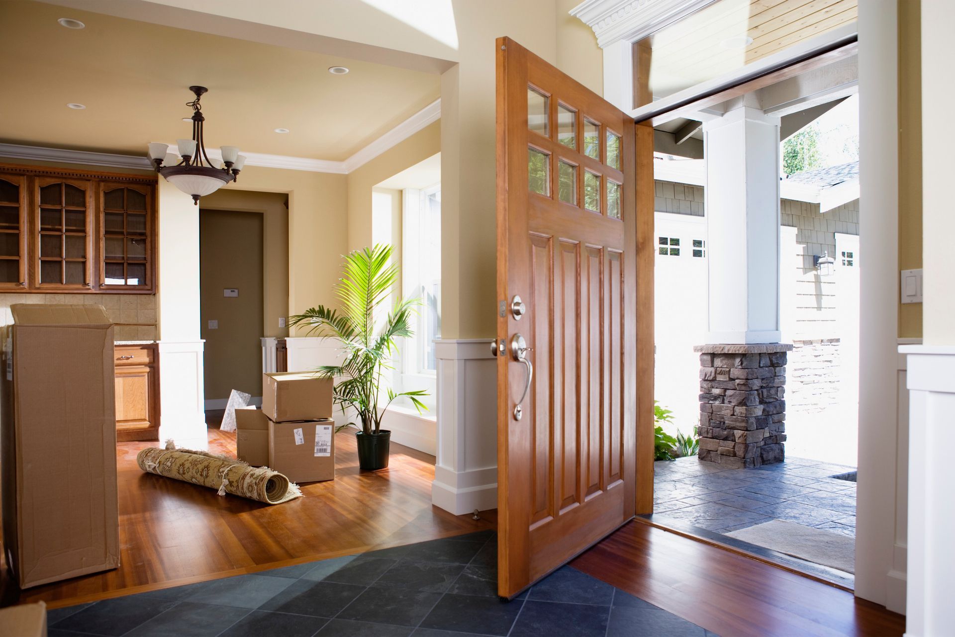 Wooden entry door with glass panes open to porch, surrounded by moving boxes and decor. Wooden entry door with glass panes open to porch, surrounded by moving boxes and decor.