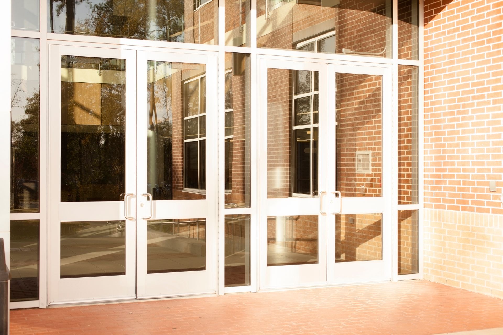White glass doors in a brick building entryway. Sunlight reflects in the windows.