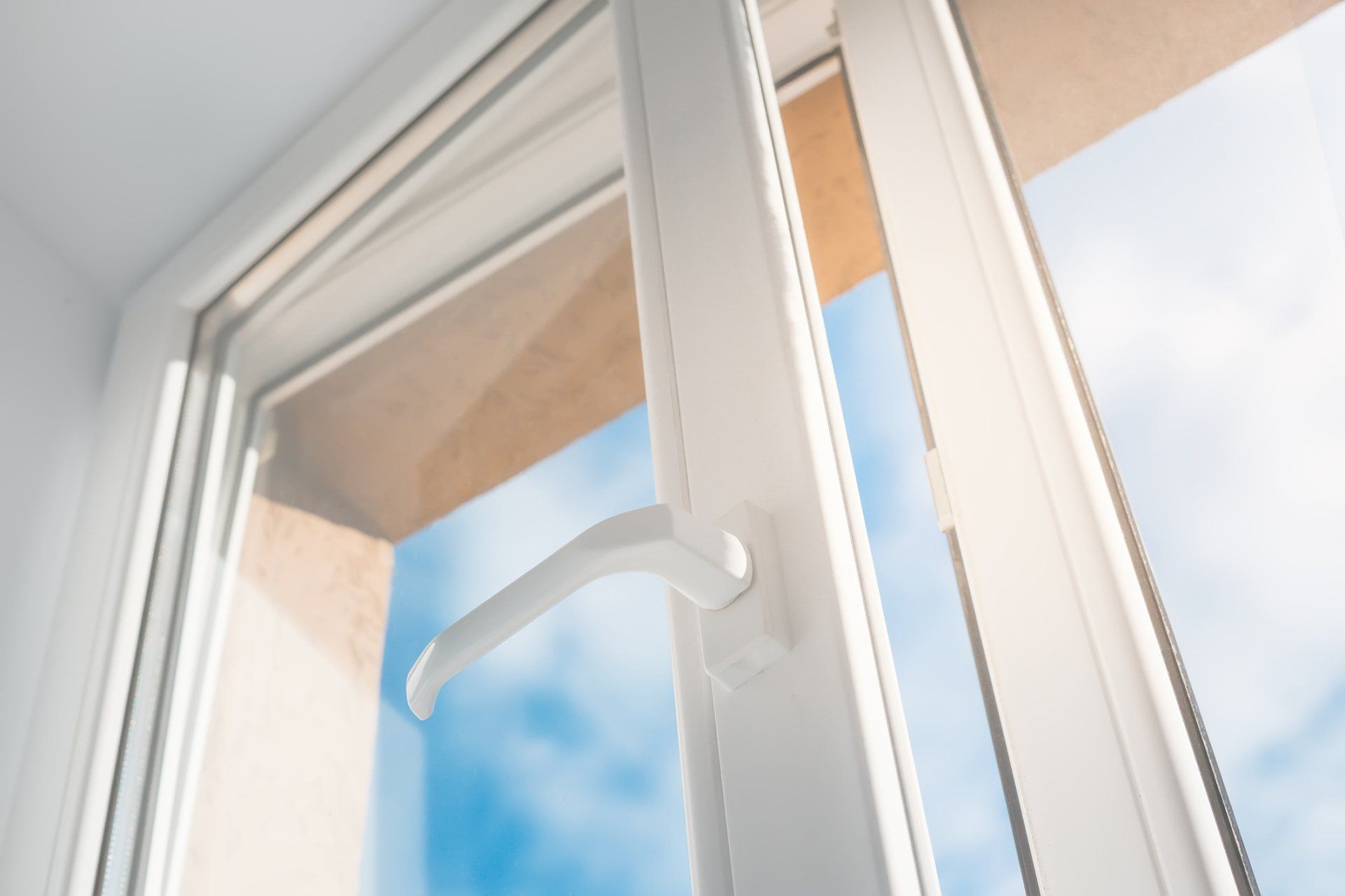 White window with handle open, against a bright blue sky and light tan wall. White window with handle open, against a bright blue sky and light tan wall.