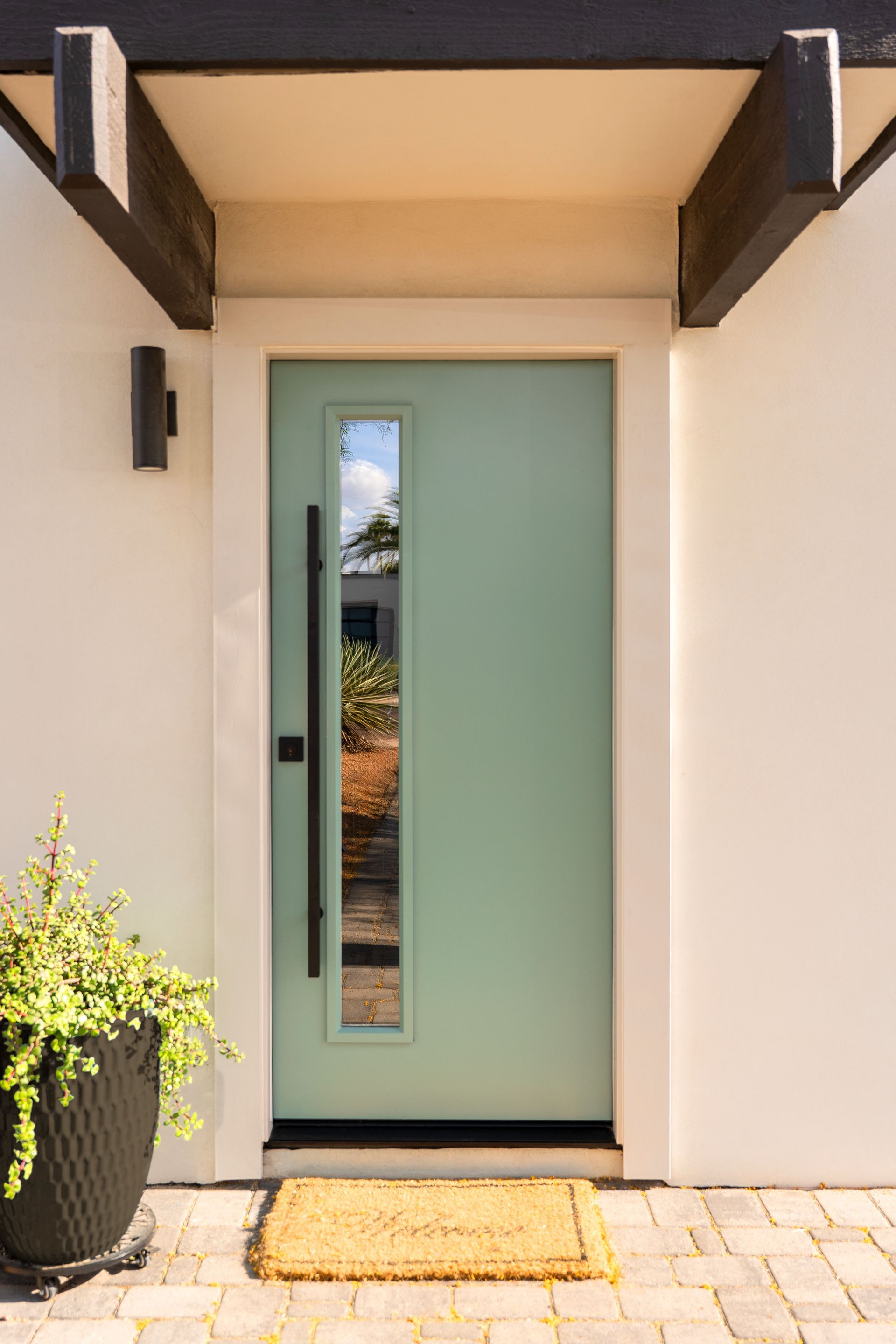 Blue front door with sidelights, brick frame, and small rug, potted plant nearby.