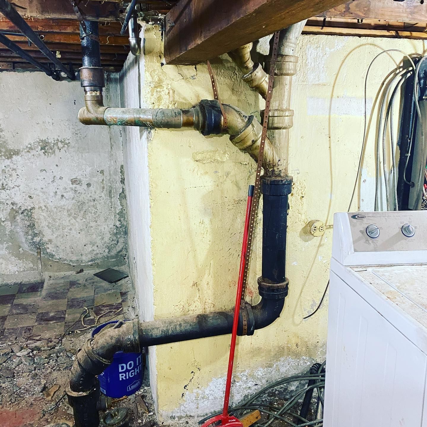 A dirty basement with a washer and dryer and pipes