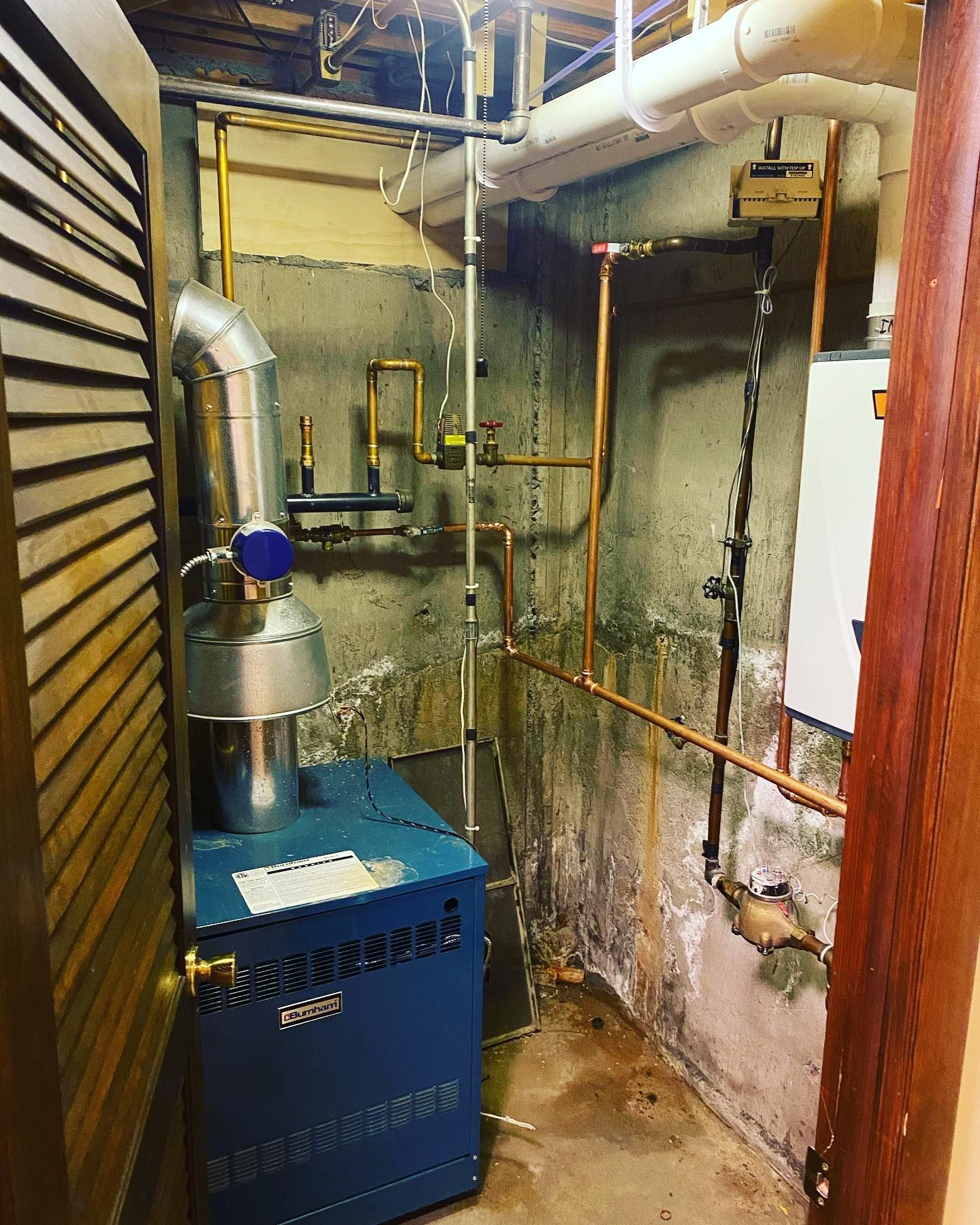 A blue boiler is sitting in a room with pipes.