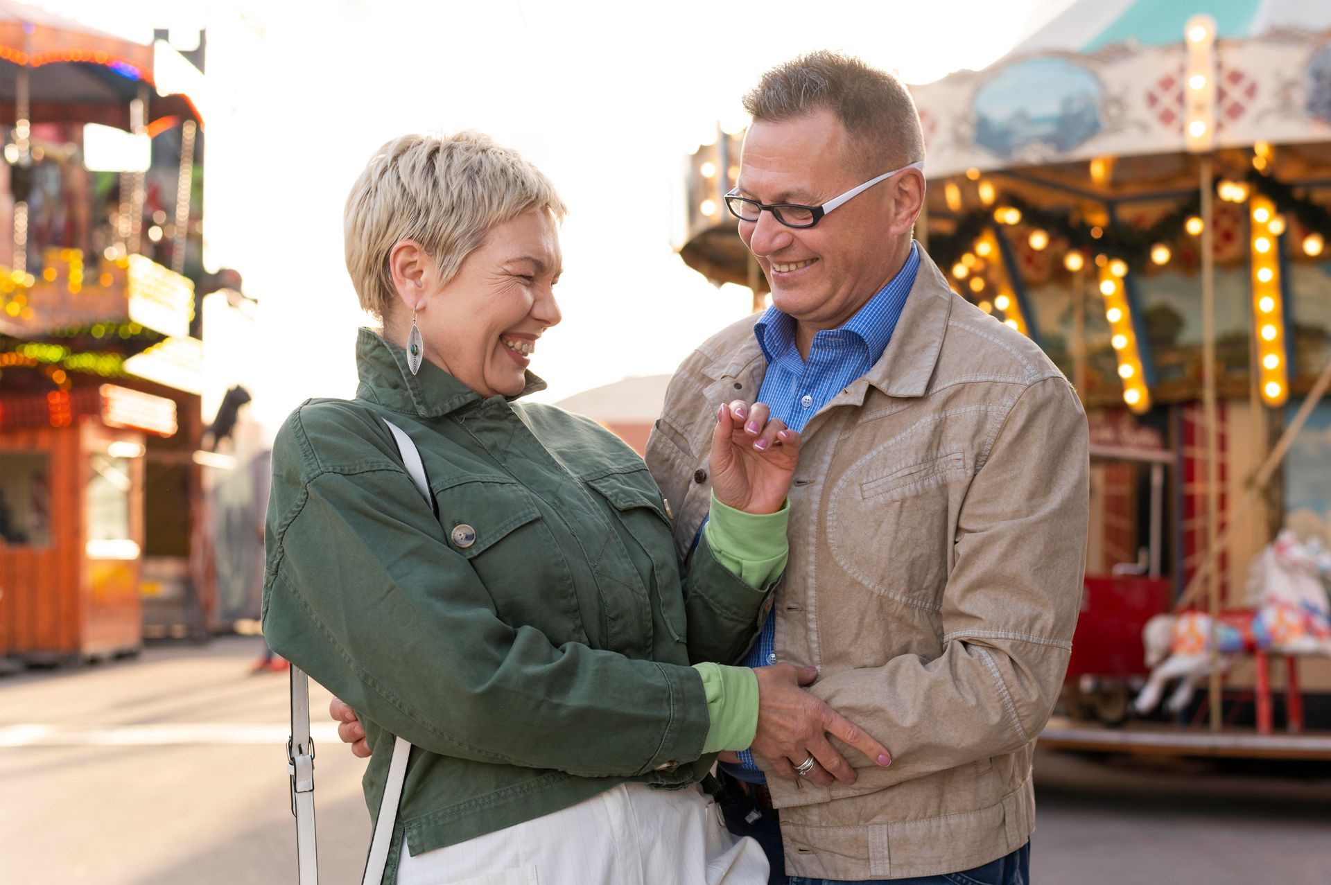A man and woman are dancing in front of a merry go round at a carnival.