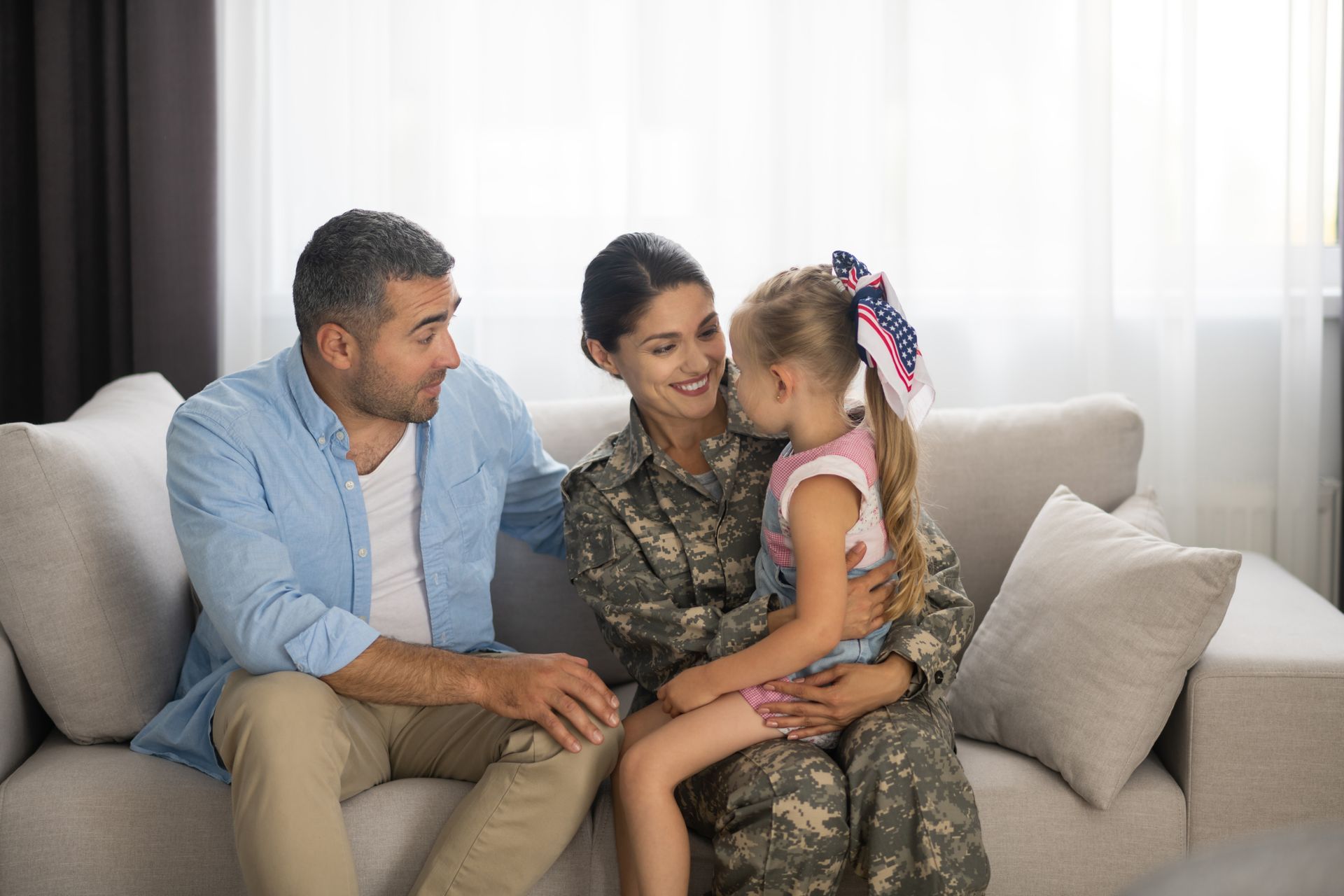 A woman in a military uniform is sitting on a couch with her husband and daughter.