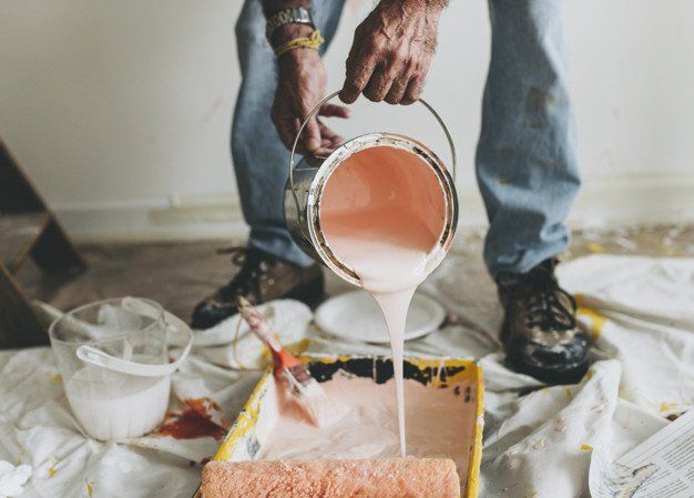 A man is pouring pink paint into a paint roller.