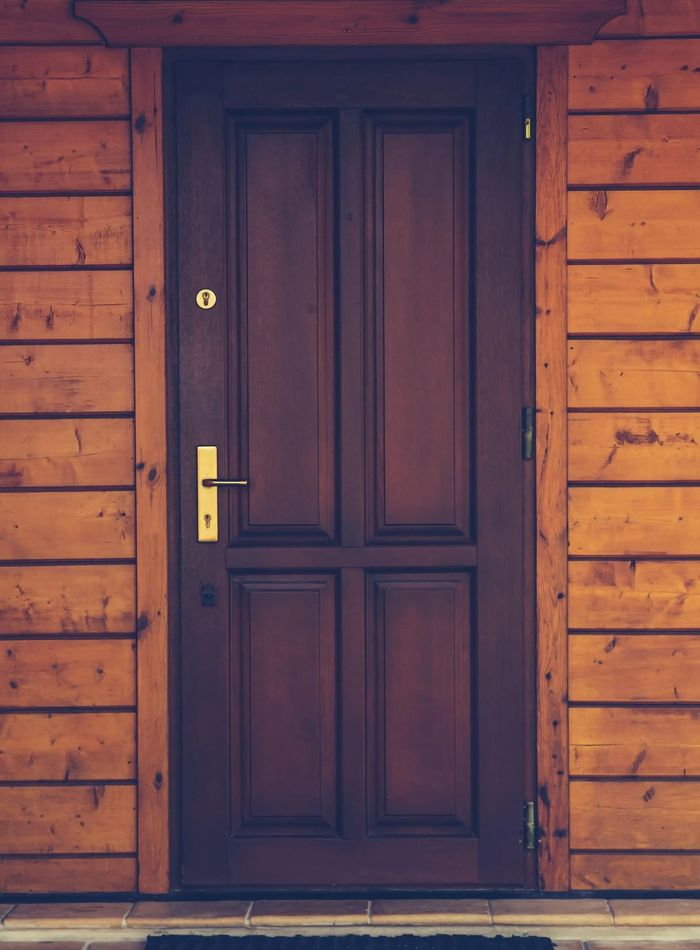 A wooden door with a black door mat in front of it.