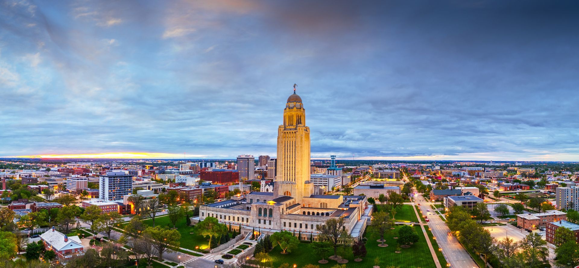Aerial view of the Nebraska State Capitol Building, lit up against a twilight sky in Lincoln, NE.
