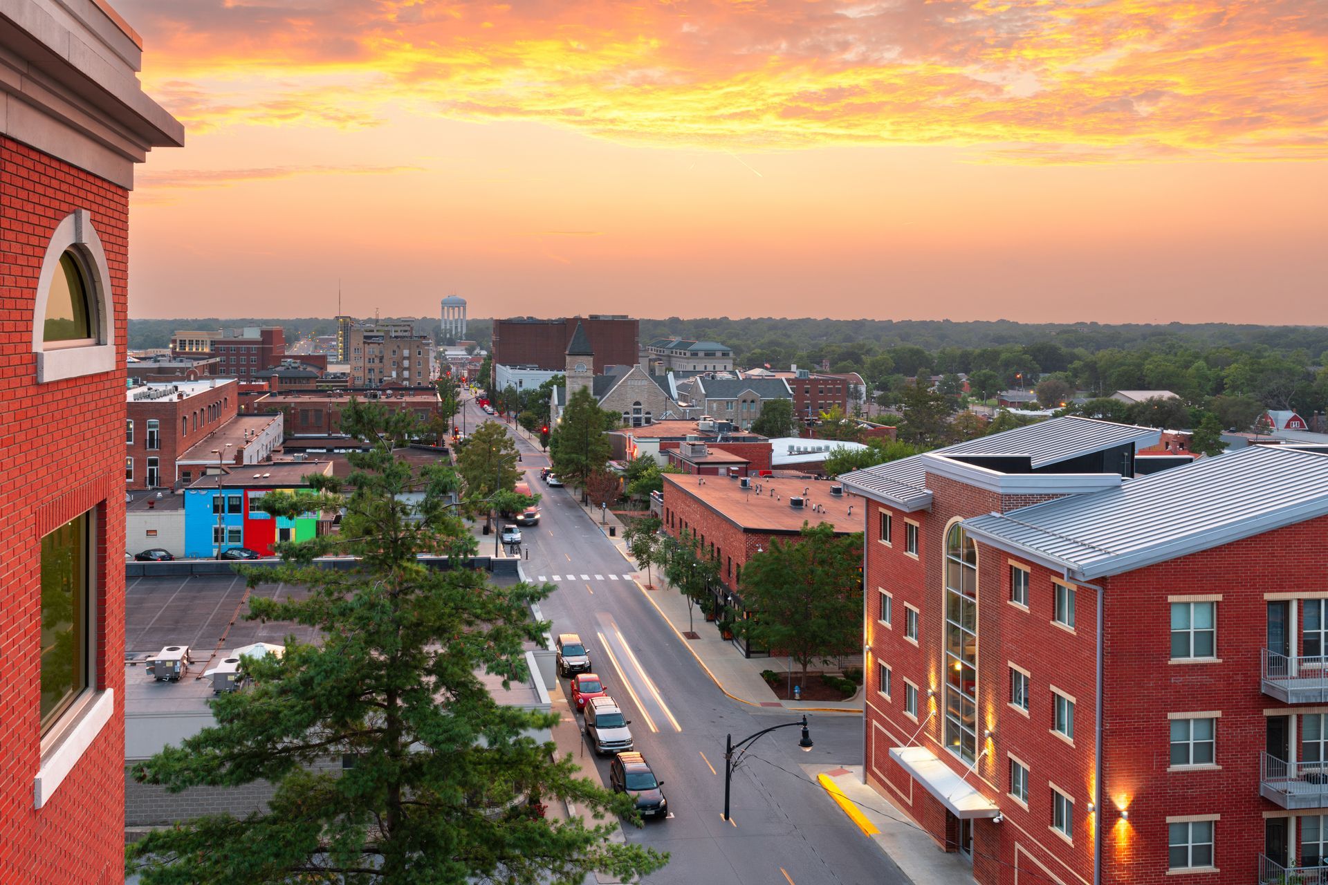 City street scene at sunset, with brick buildings lining the road and an orange sky.