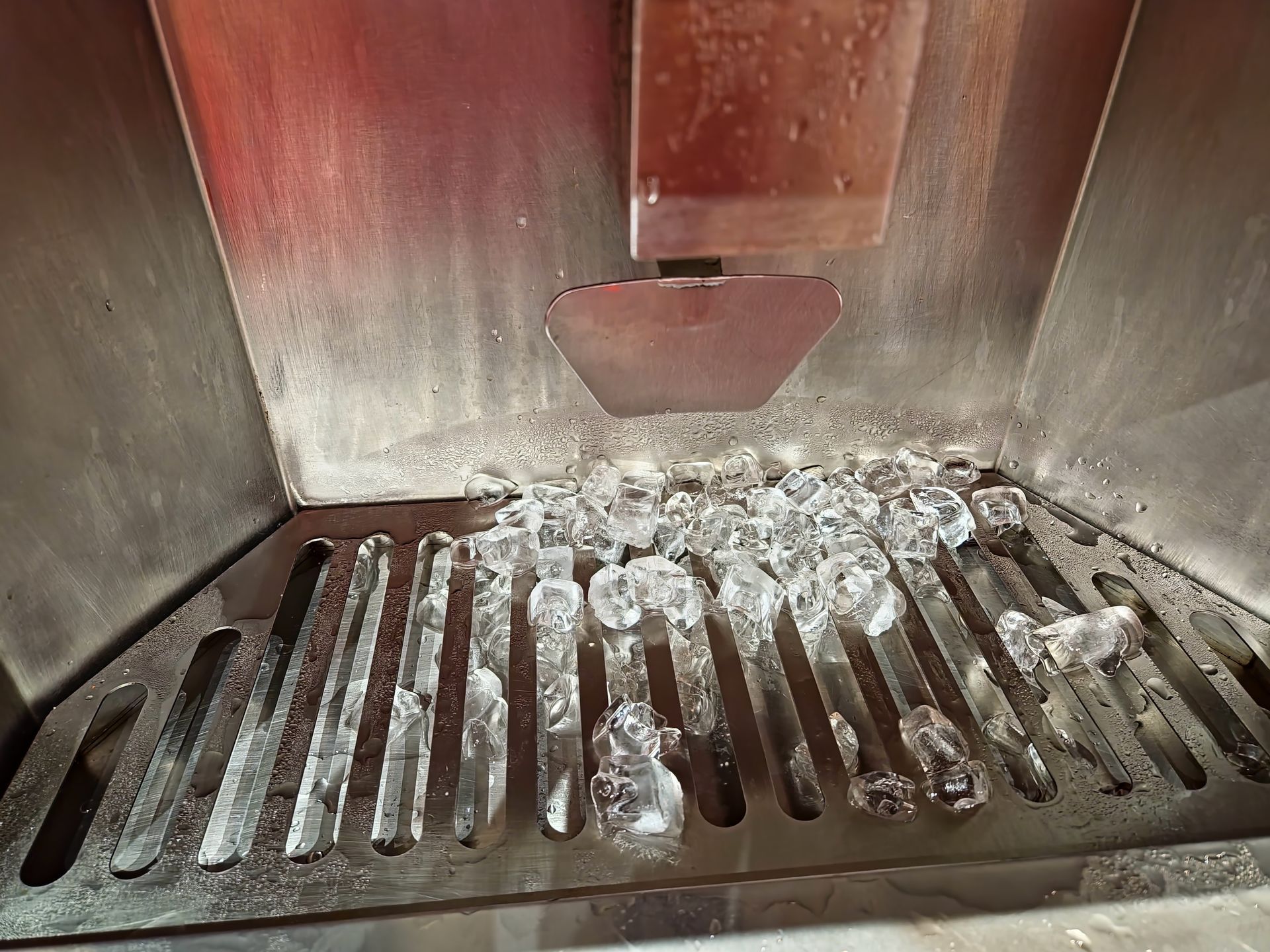Ice machine dispensing ice cubes onto a metal grate.